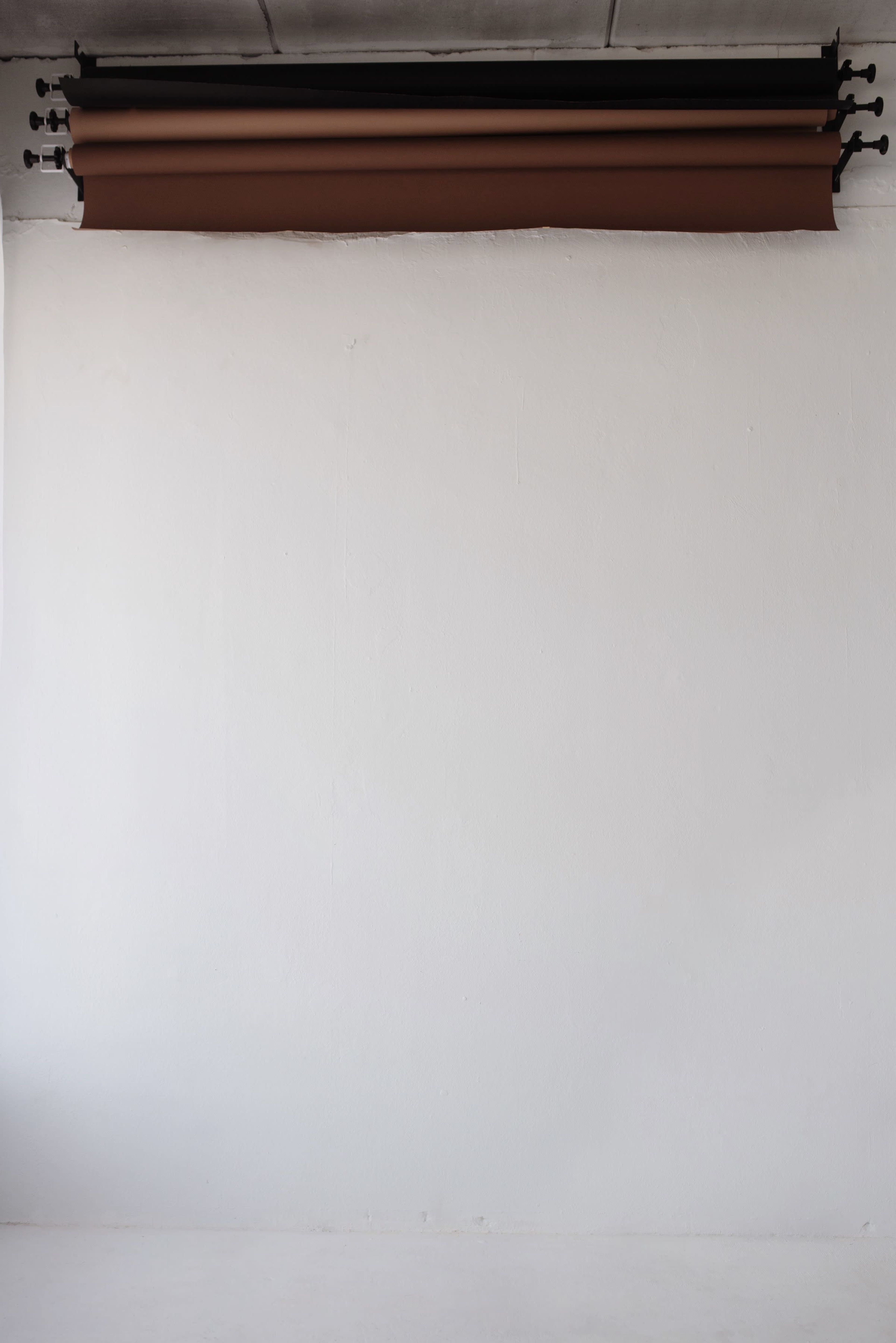 A white wall with rolled-up brown backdrop paper mounted at the top.