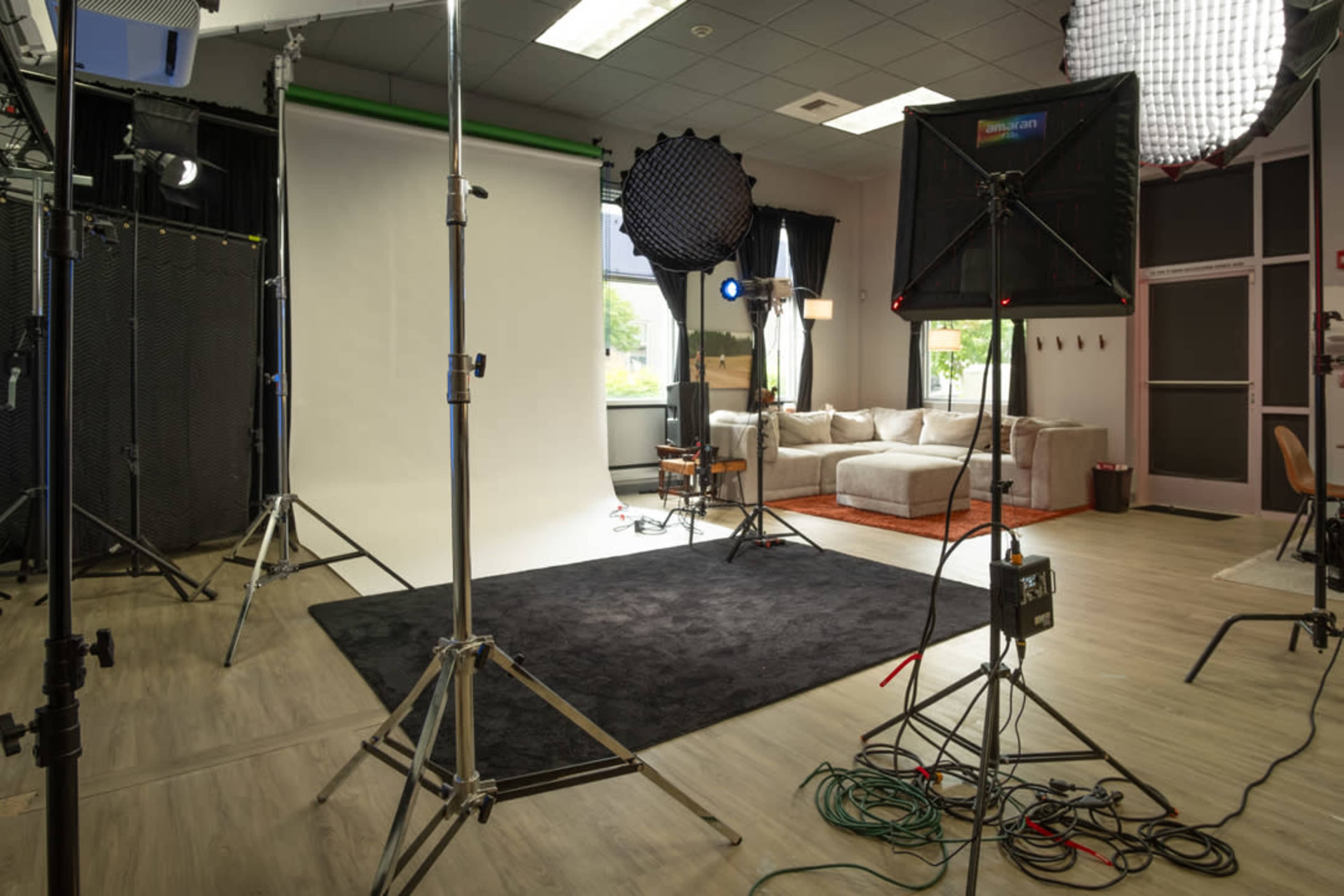 The image shows a photography studio equipped with lighting setups, a blank backdrop, and a seating area.