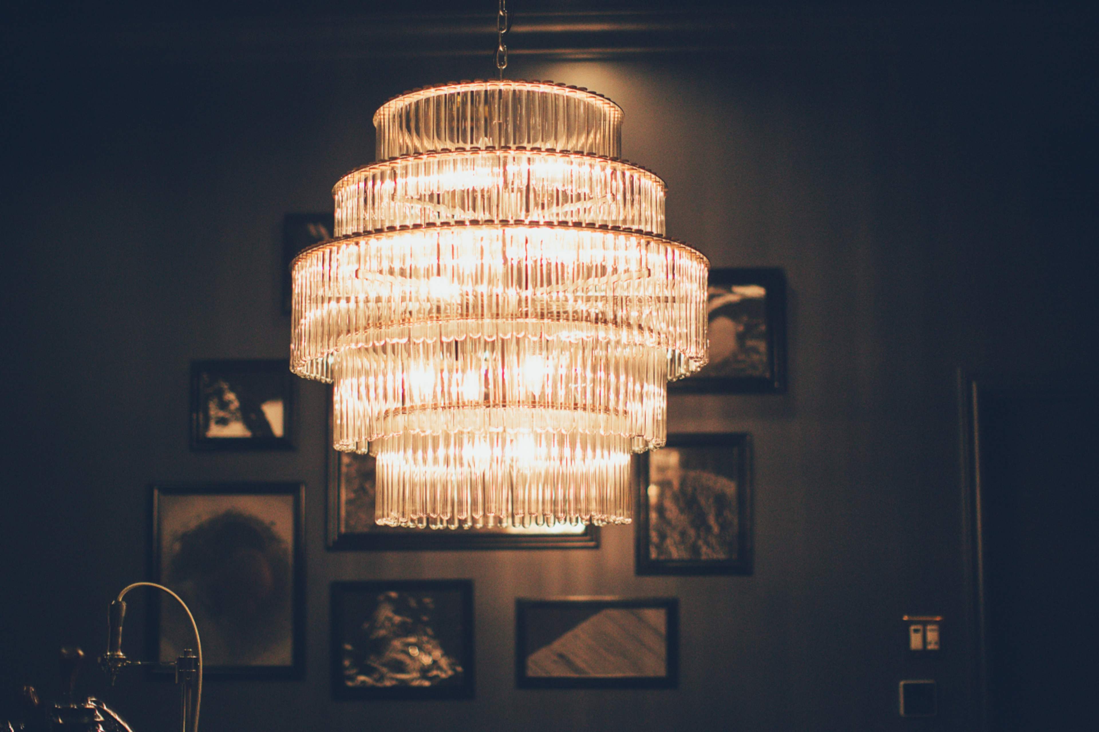 A multi-tiered glass chandelier hangs from the ceiling against a backdrop of framed images on the wall.