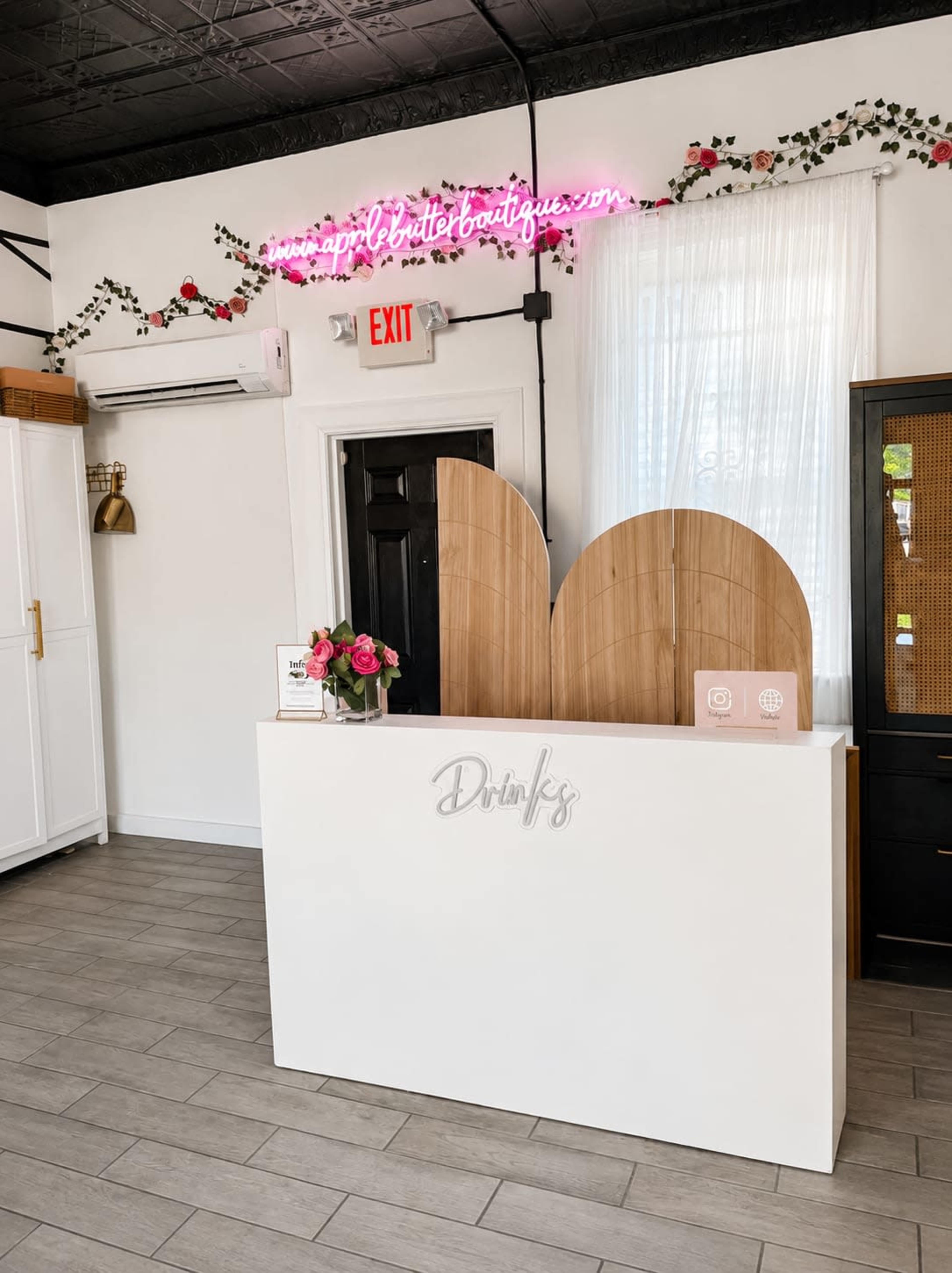 The image shows a modern reception area with a white counter, pink neon sign, and floral wall decor.