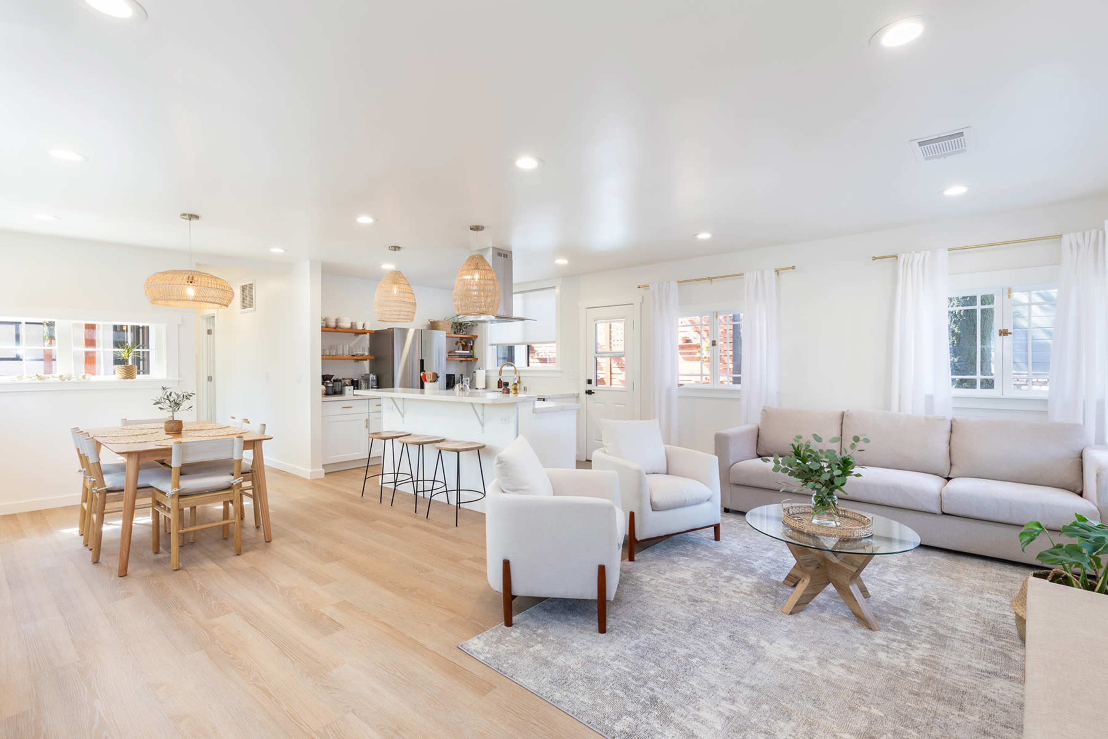 A modern, open-concept living space with a light-colored sofa, a dining area, and a kitchen visible in the background.