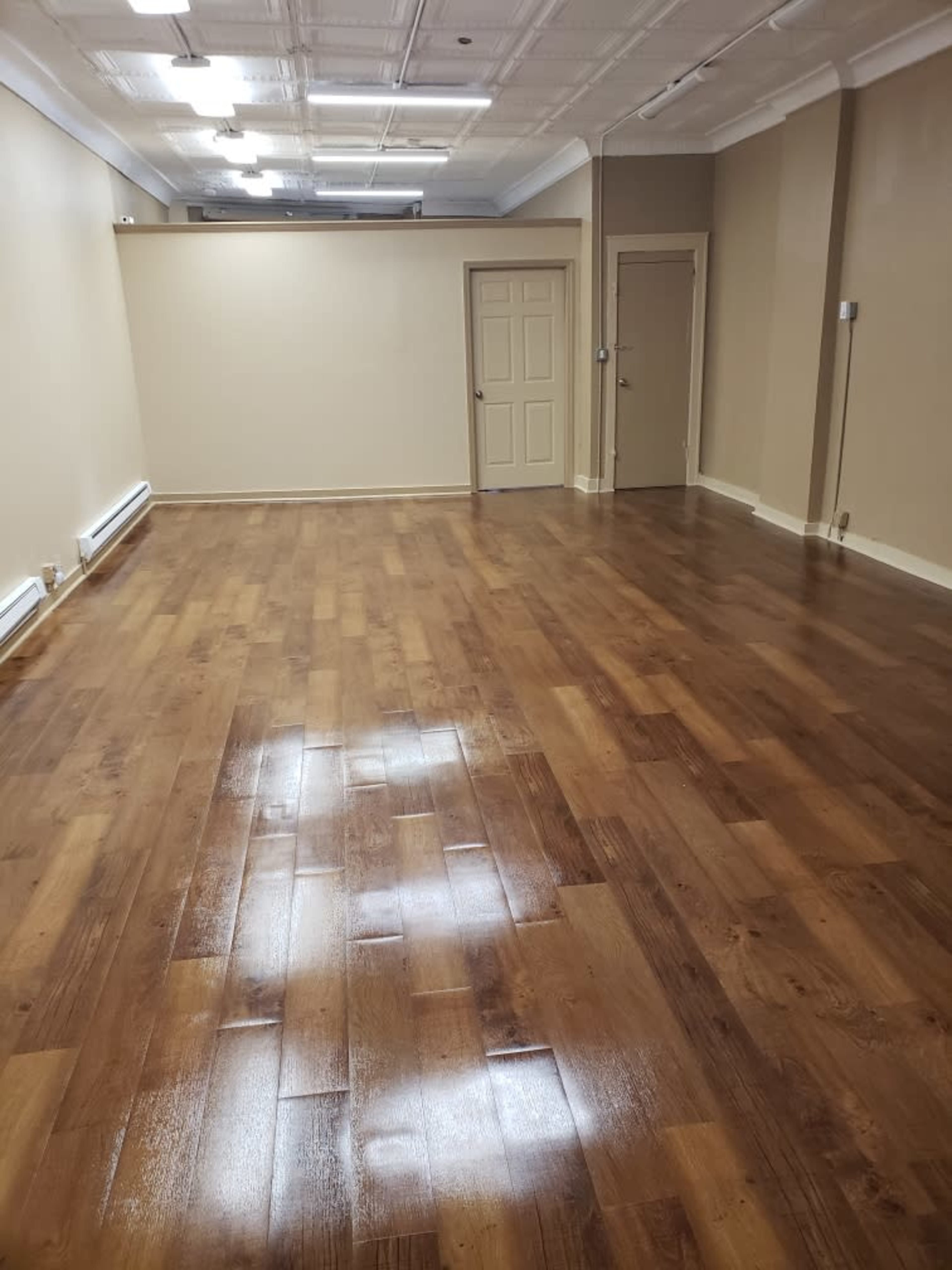 A spacious, empty room with polished wooden flooring and neutral-colored walls.