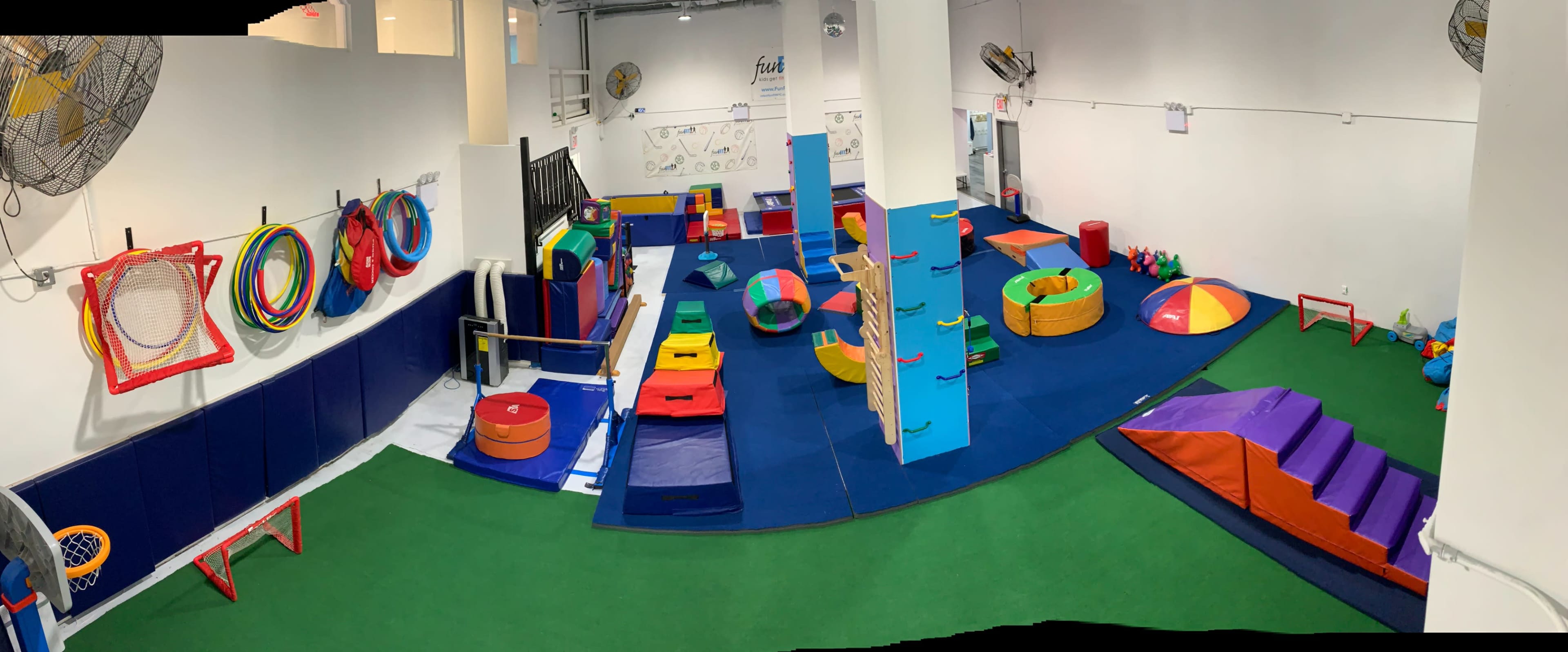 The image shows a brightly colored indoor play area equipped with various shapes and structures for children's physical activities, including climbing sections, soft mats, and play equipment.