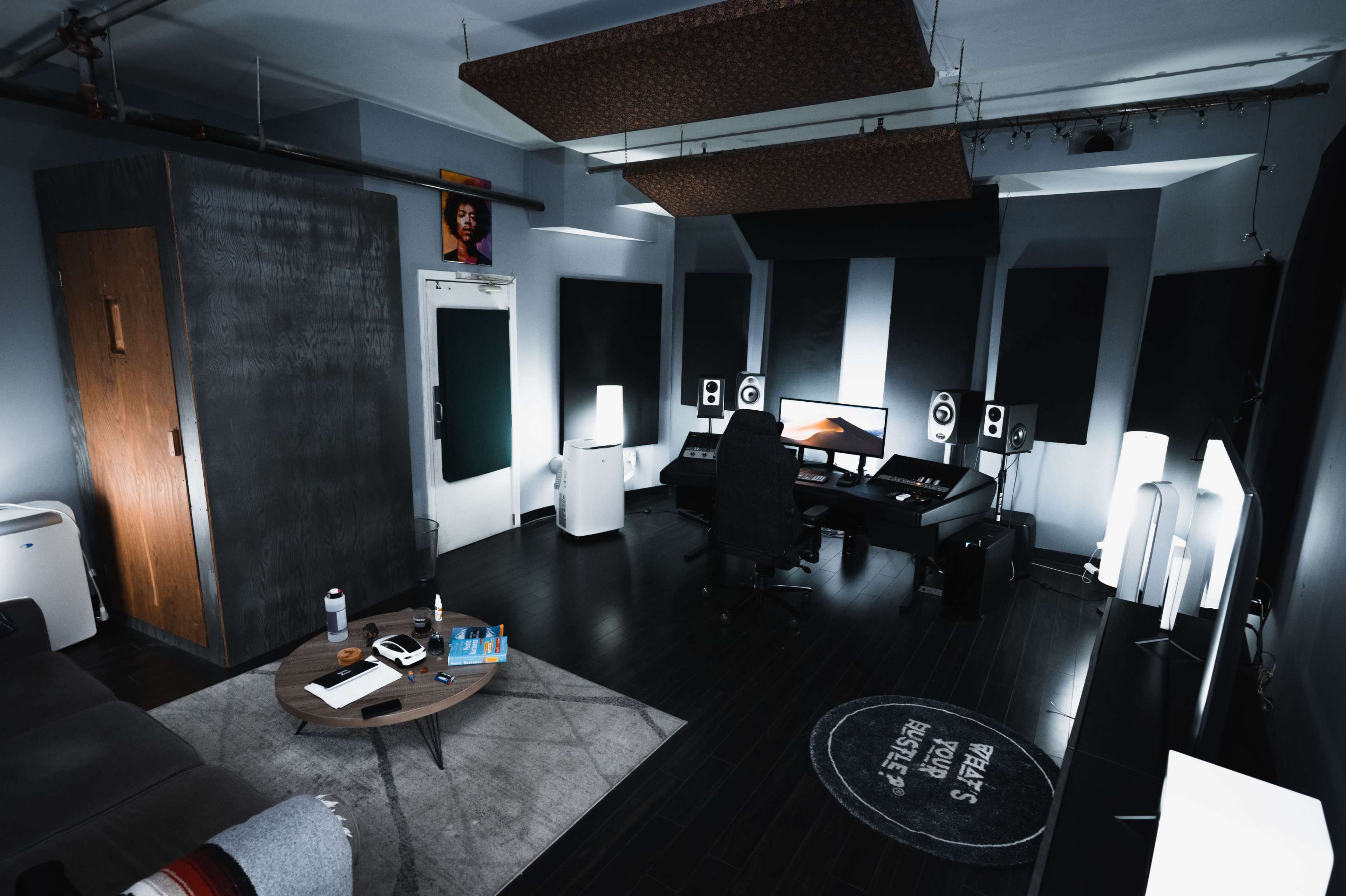 A modern music studio featuring a black desk with audio equipment, two large monitors, and ambient lighting in a dimly lit room.