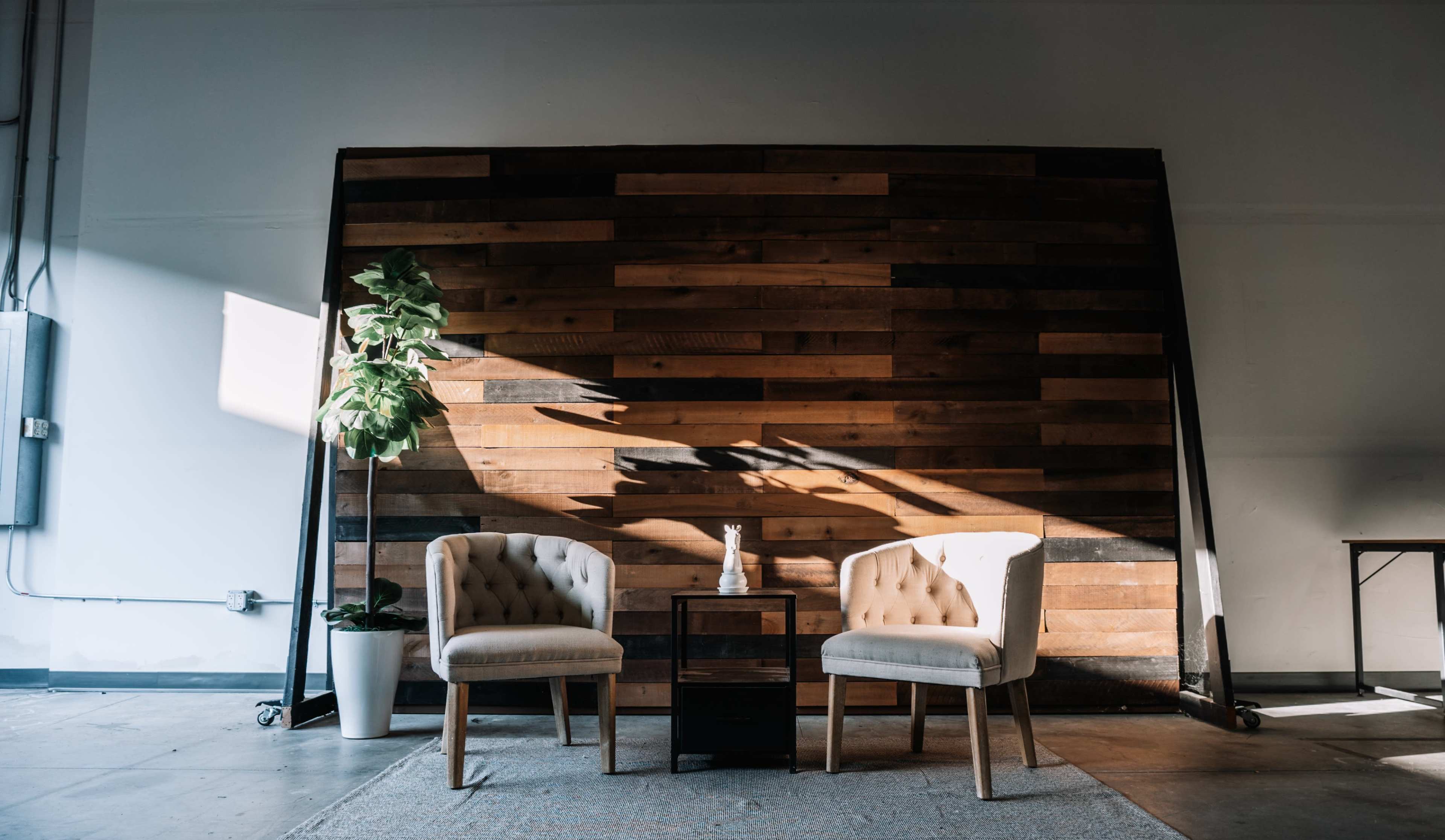 Two upholstered chairs are positioned in front of a wooden accent wall, accompanied by a small table and a potted plant.