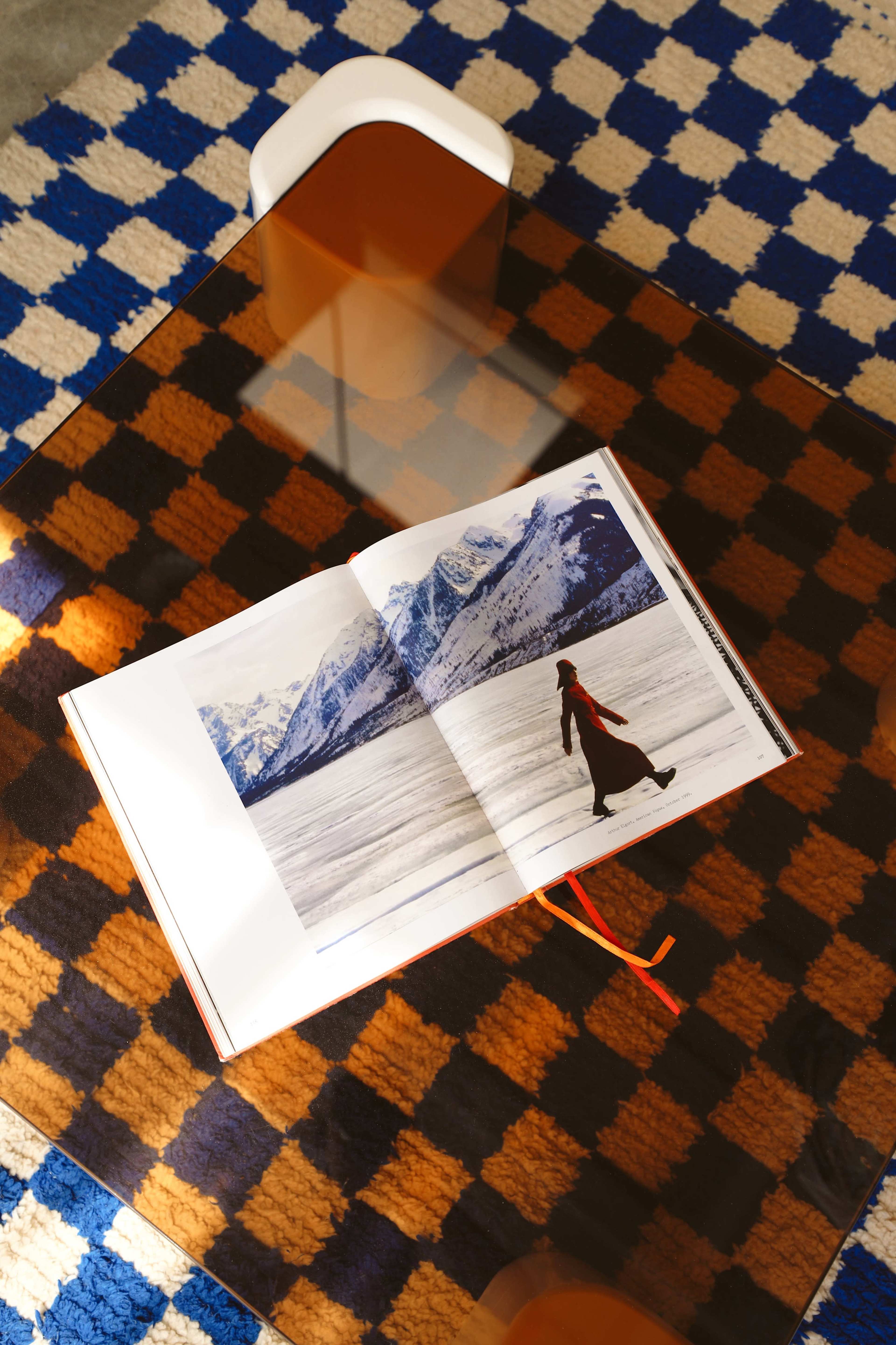 An open magazine featuring a photograph of a person walking on a snowy landscape is displayed on a glass table over a patterned rug.