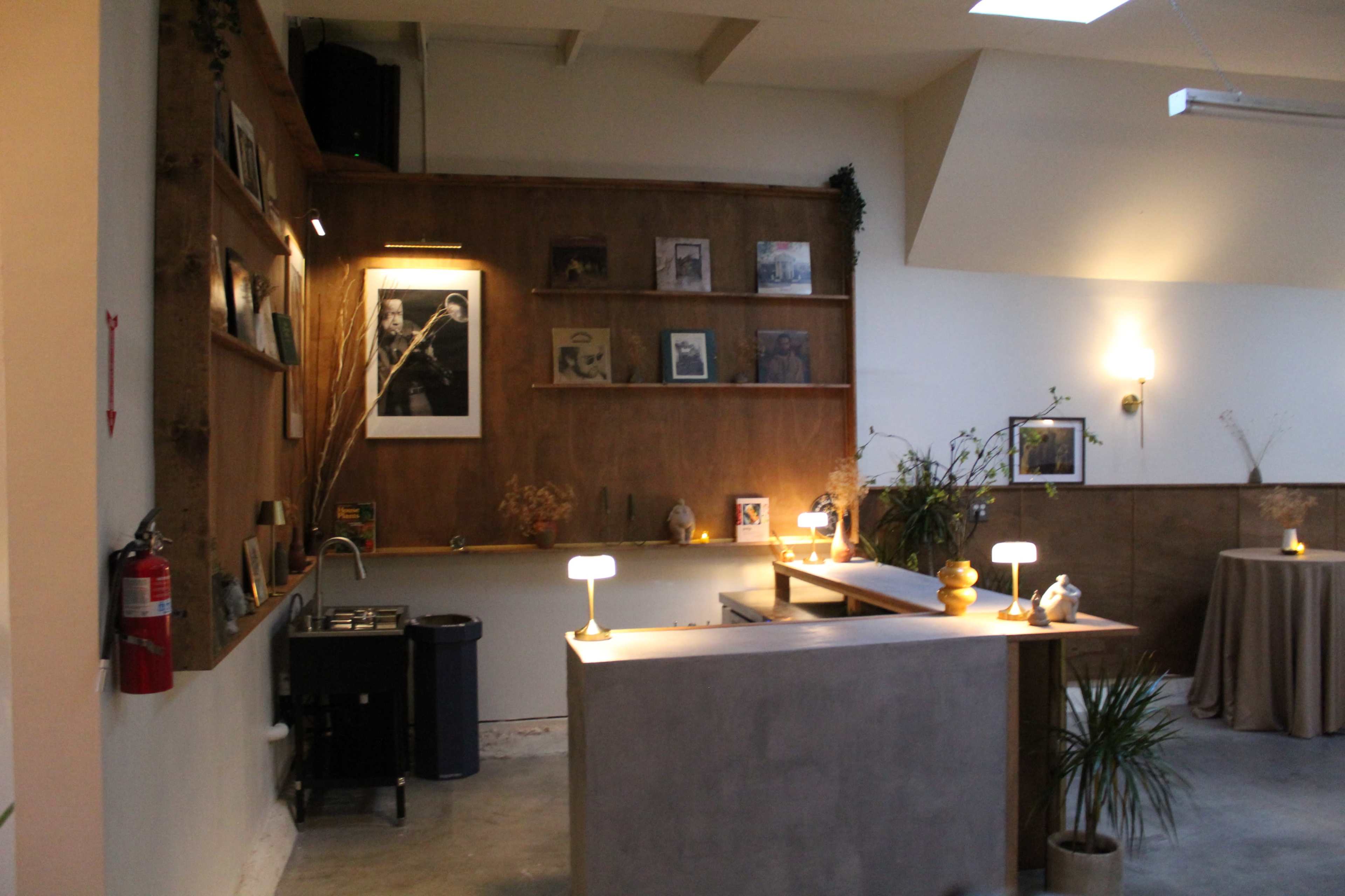 The image shows a cozy café interior with a wooden counter, shelves displaying framed photos, and warm lighting.