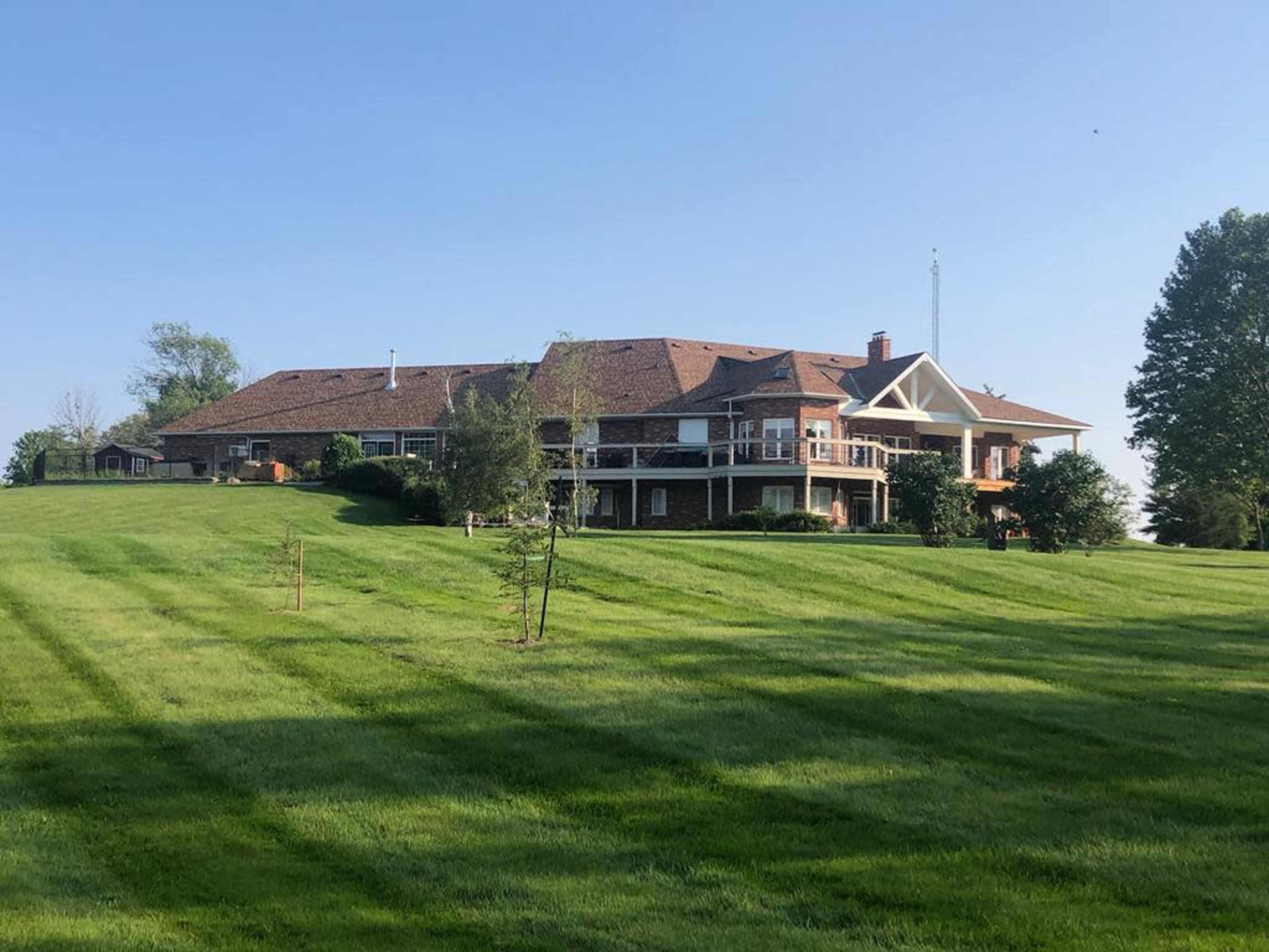 A large brick house with a sloped roof and multiple balconies is situated on a lush green hillside.