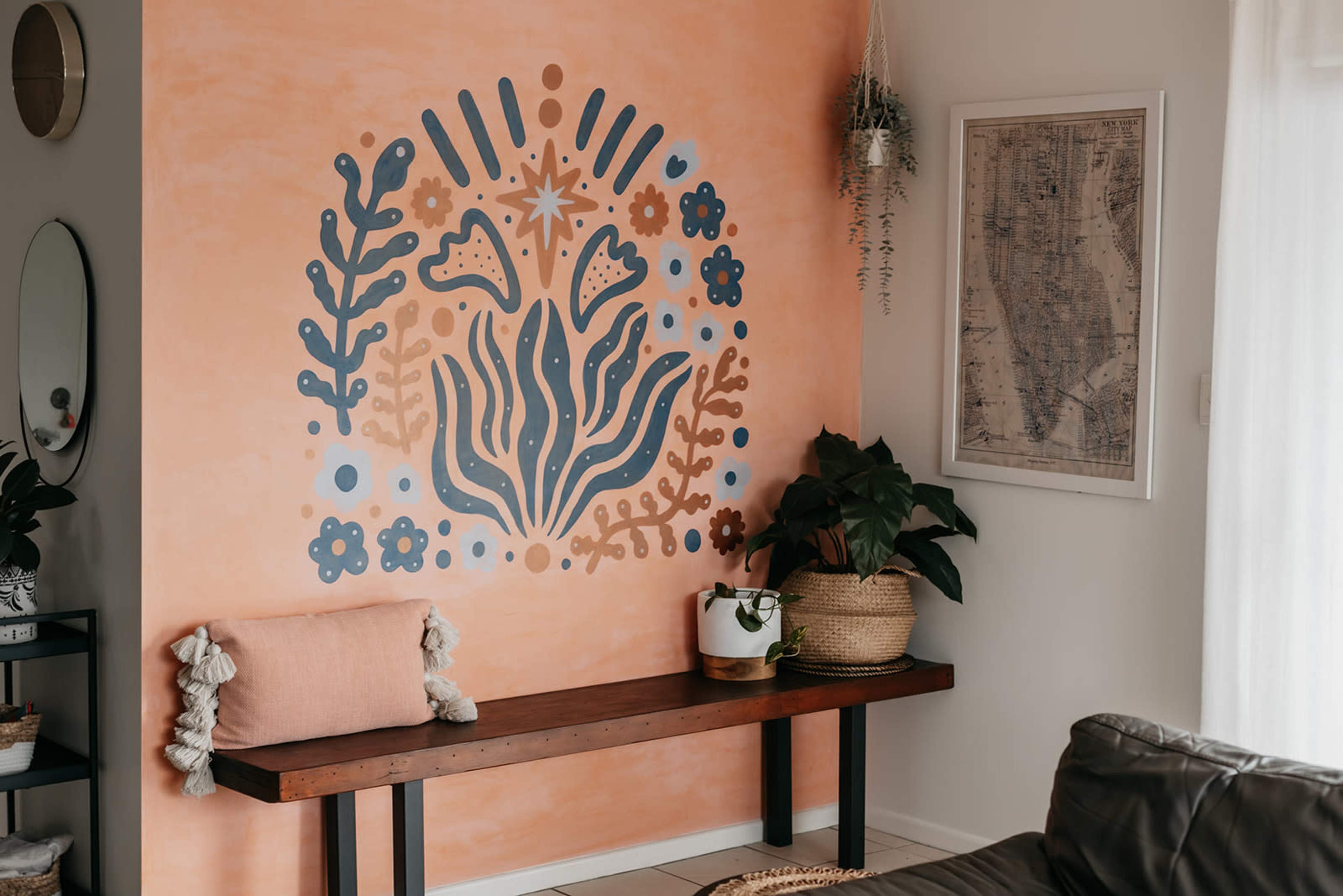 A living room corner with an orange wall decorated with a floral mural, a wooden bench, a potted plant, and a framed map on the adjacent wall.