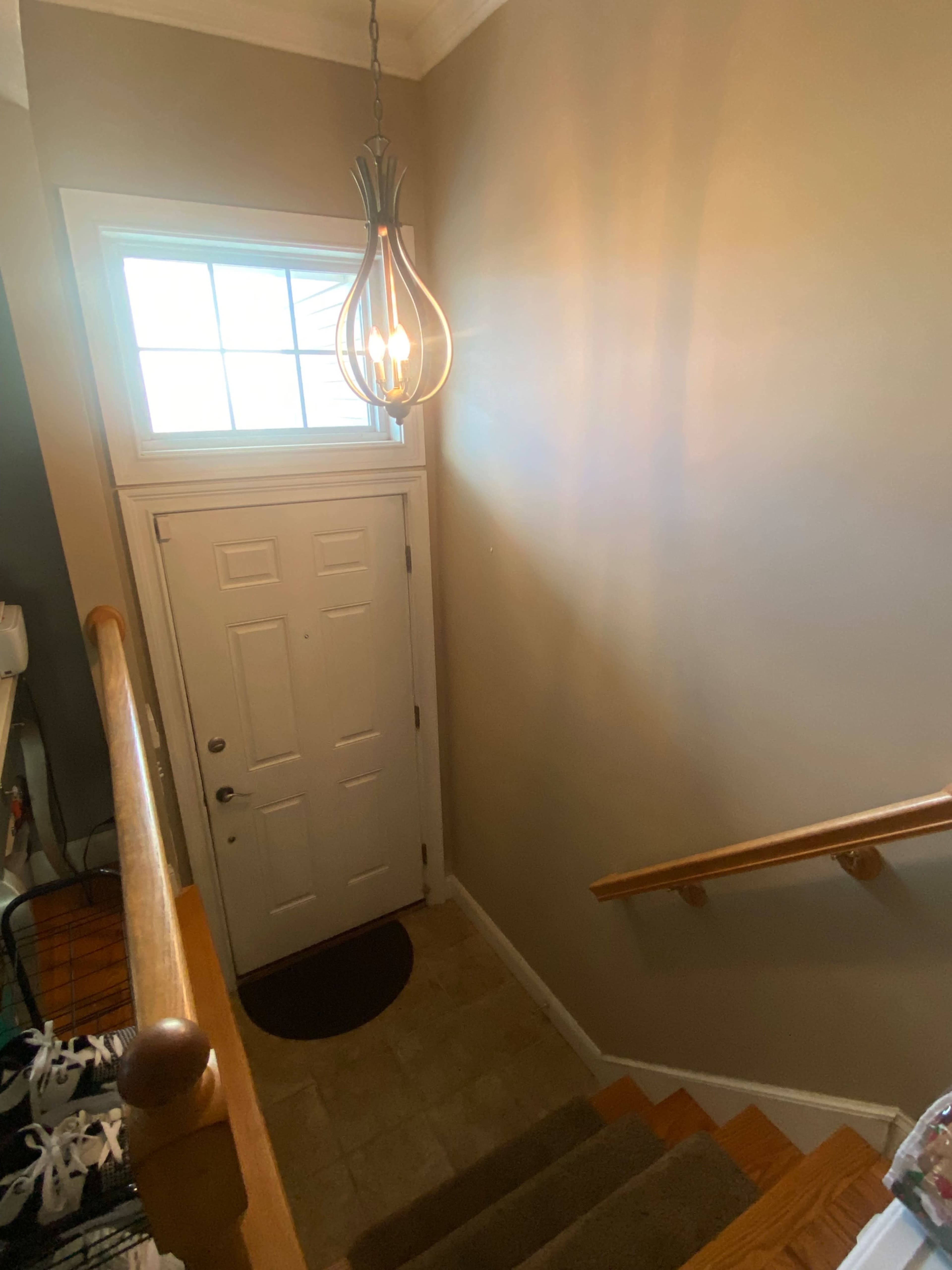 A staircase leads to a front door located beneath a window, illuminated by a hanging light fixture.