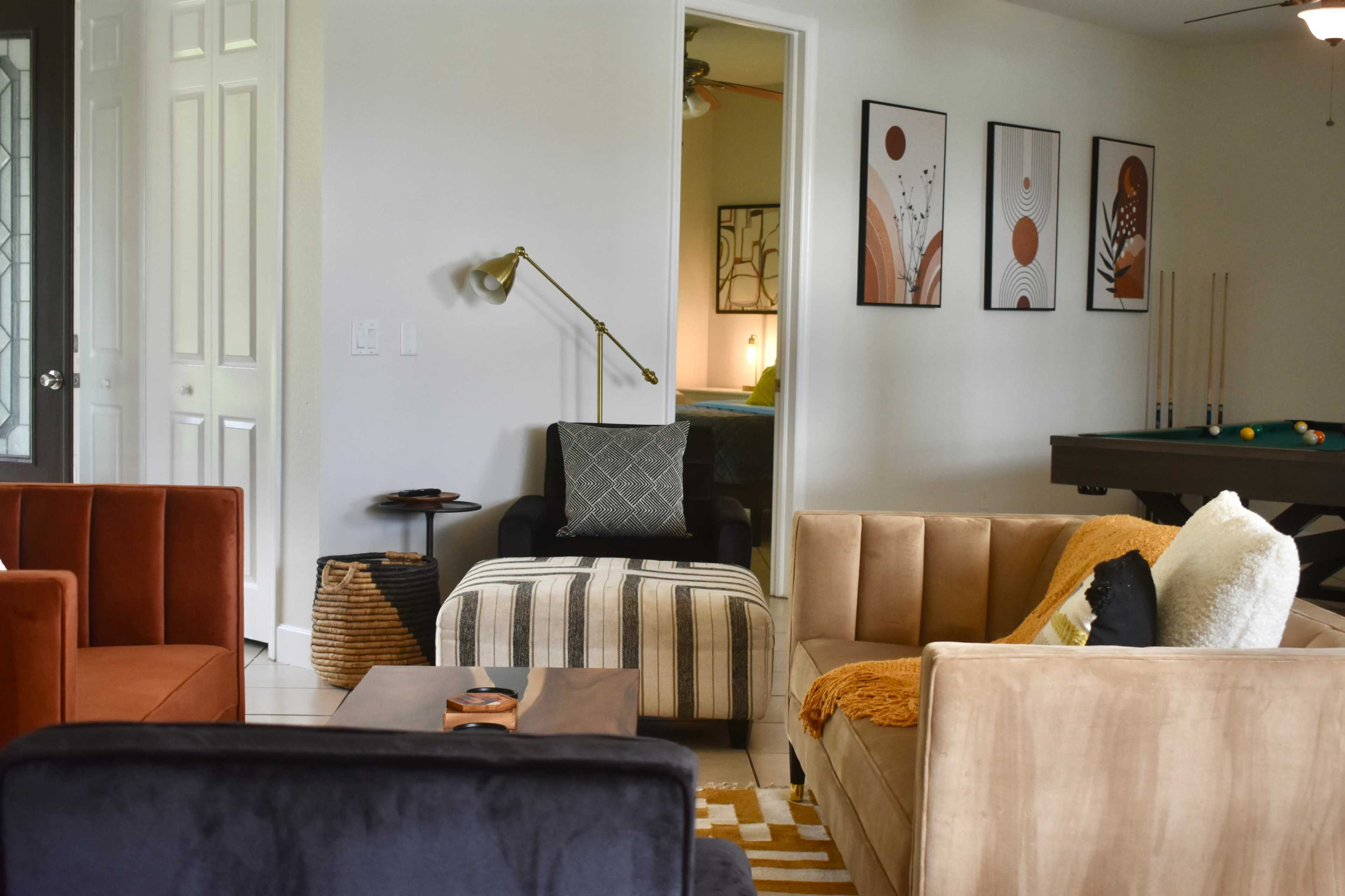 A modern living room with various seating options, including a striped ottoman and chairs, alongside wall art and a doorway leading to another room.
