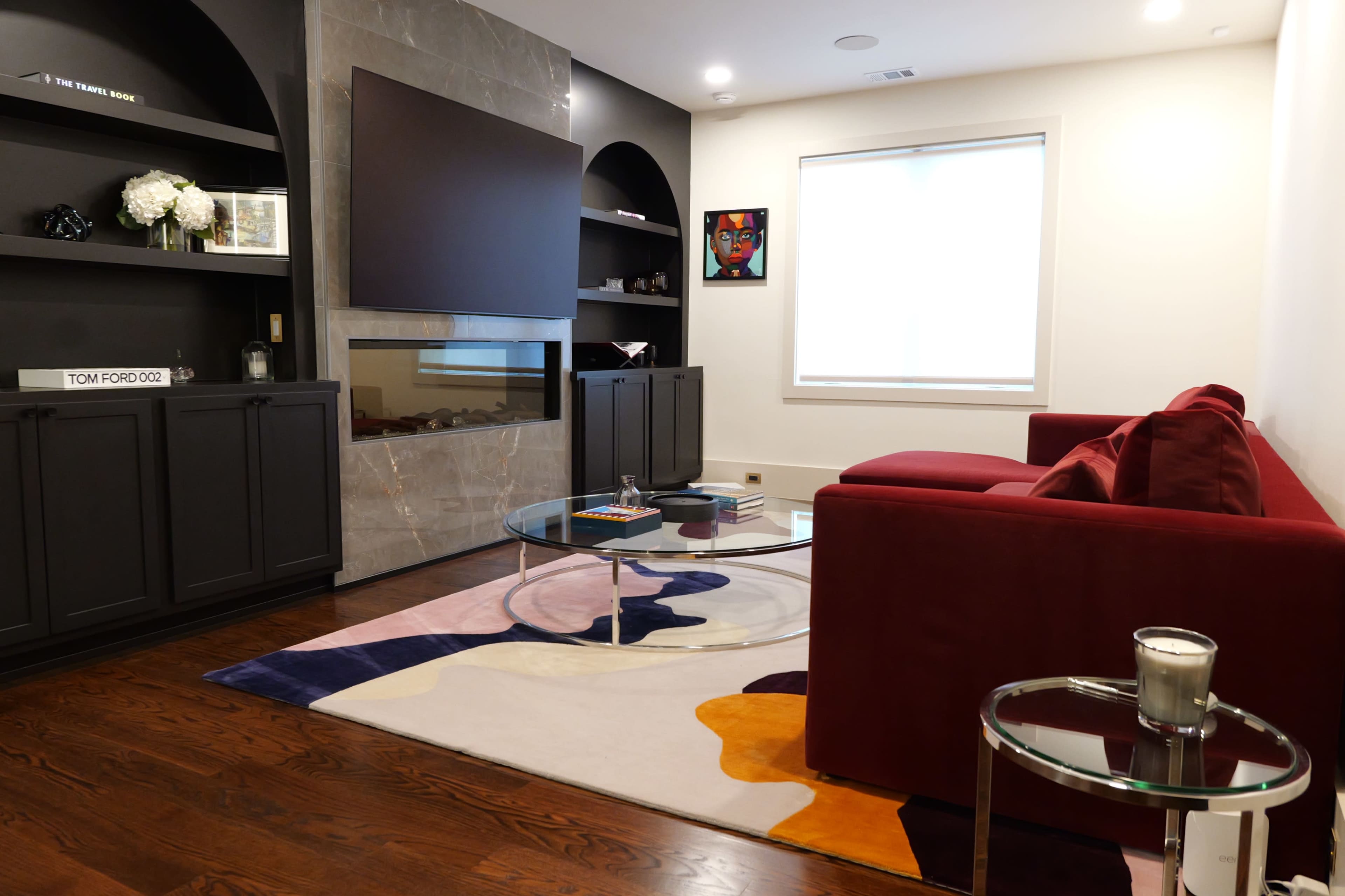 The image shows a modern living room with a red sofa, a circular glass coffee table, and a large television mounted on a dark accent wall.