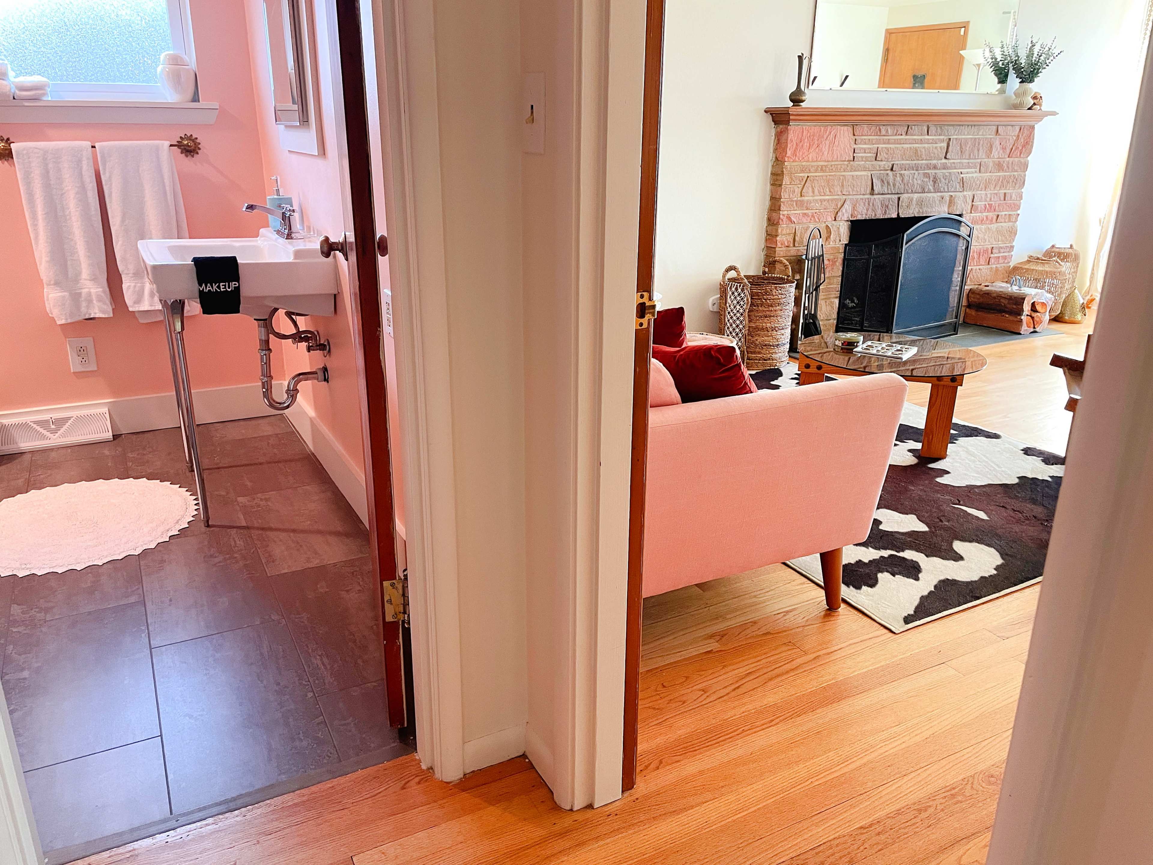 A doorway leads from a bathroom with a sink to a living room featuring a couch, coffee table, and a fireplace.
