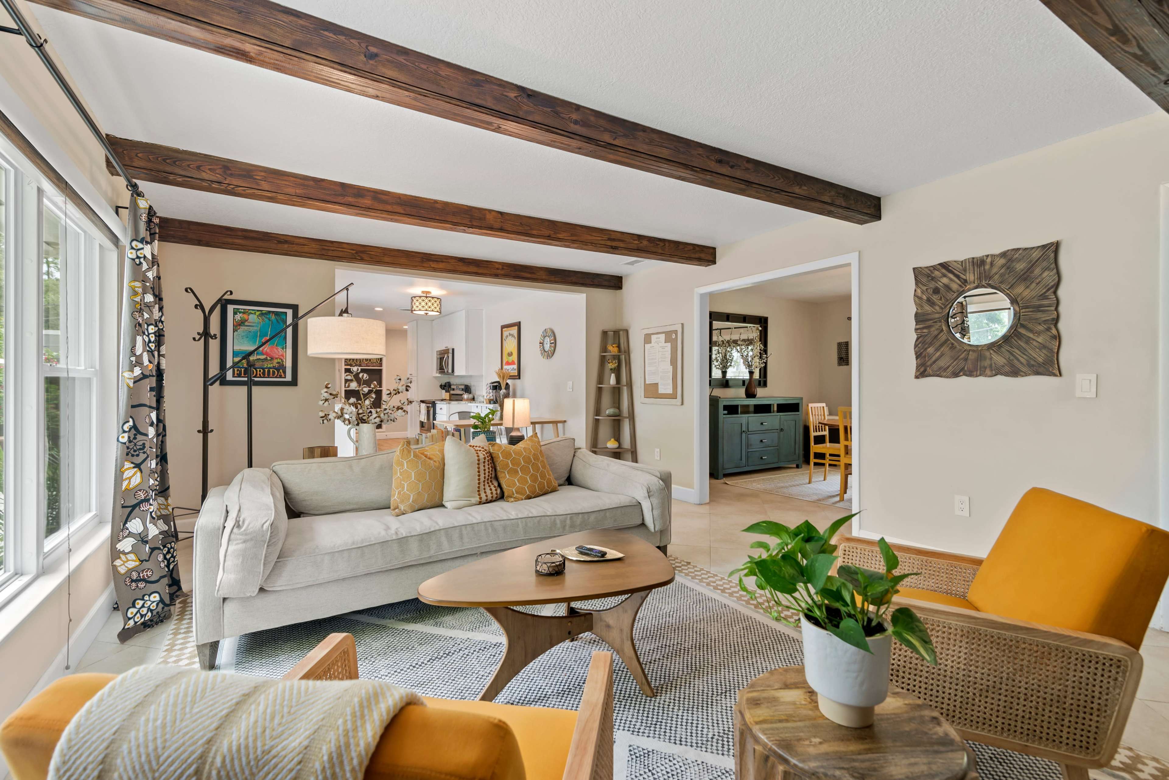 The image shows a living room with a light gray sofa, yellow armchairs, a wooden coffee table, and exposed wooden beams on the ceiling.