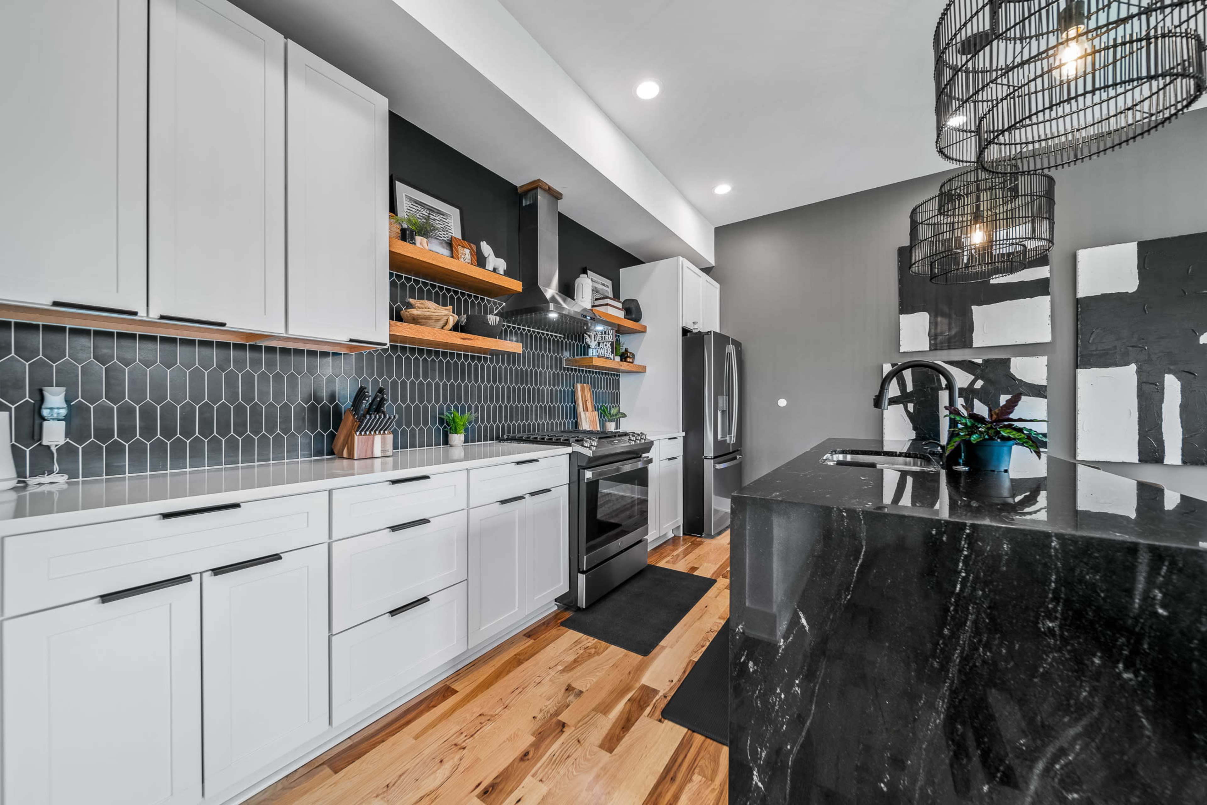 A modern kitchen features white cabinetry, a black stone island, and hexagonal tile backsplash.
