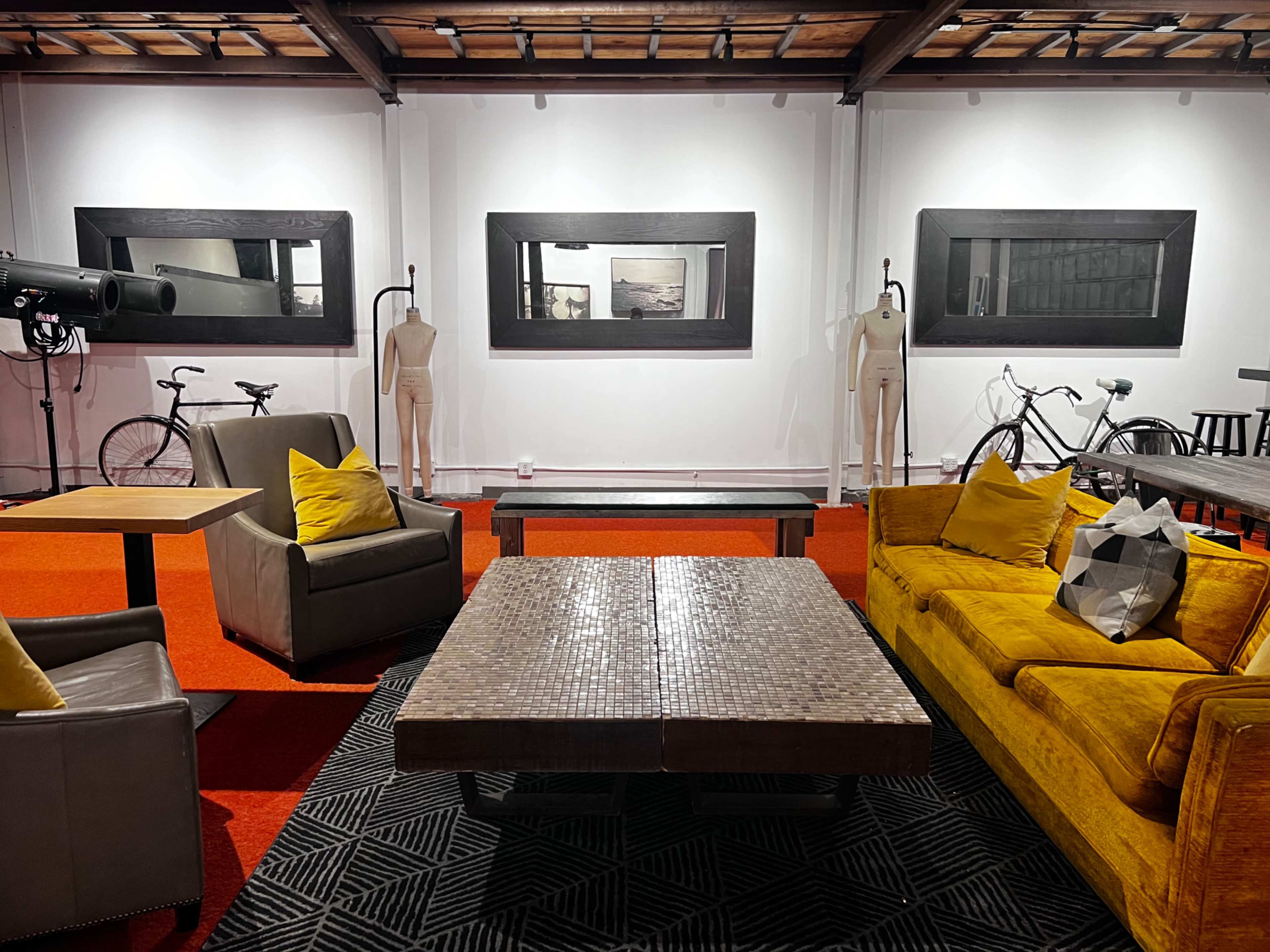 The image shows a modern, open lounge area with two couches, a large coffee table, and several bicycles hanging on the walls, accompanied by artistic mirrors and mannequins.