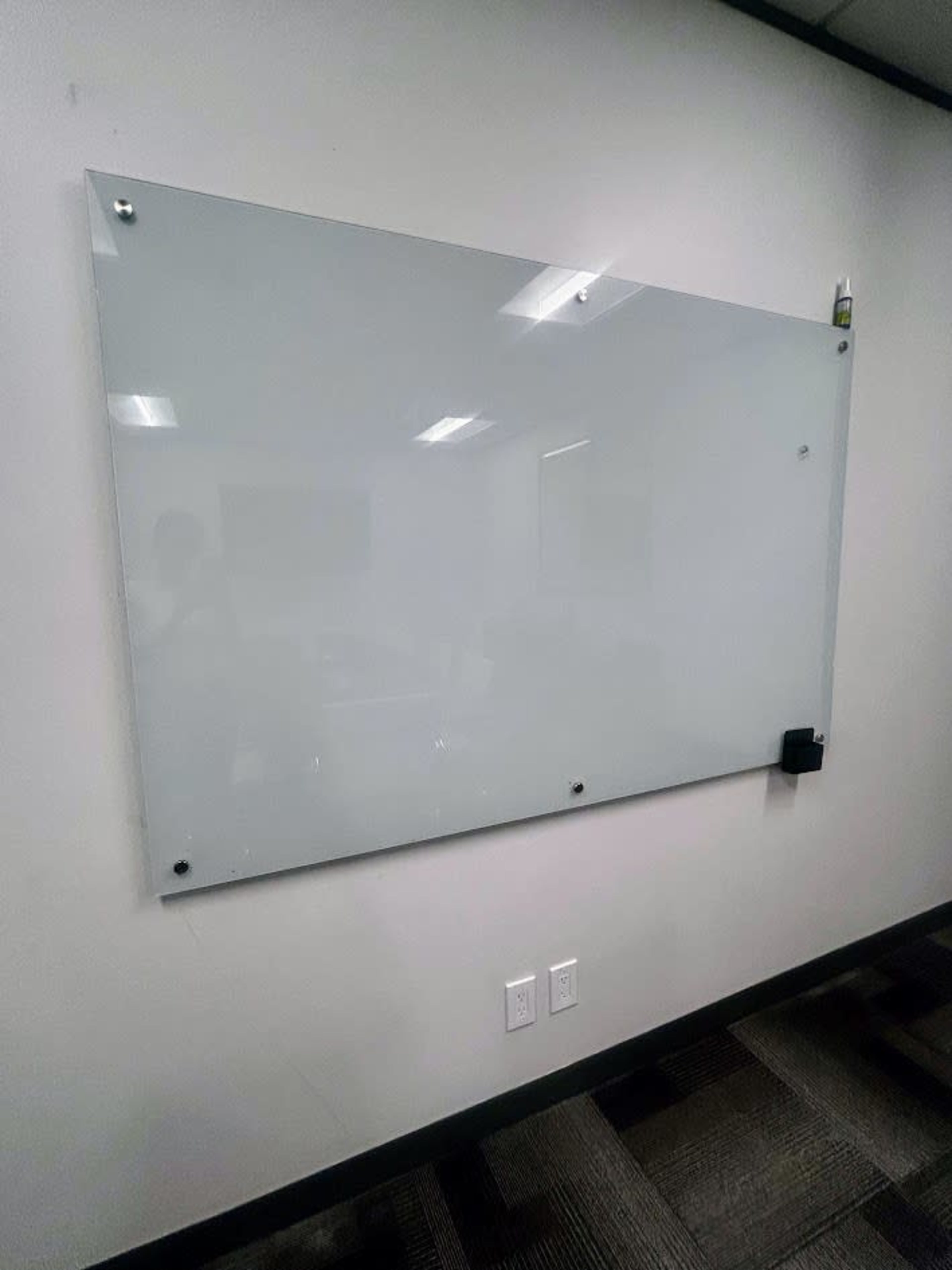 A clear glass whiteboard is mounted on a wall in an office environment.