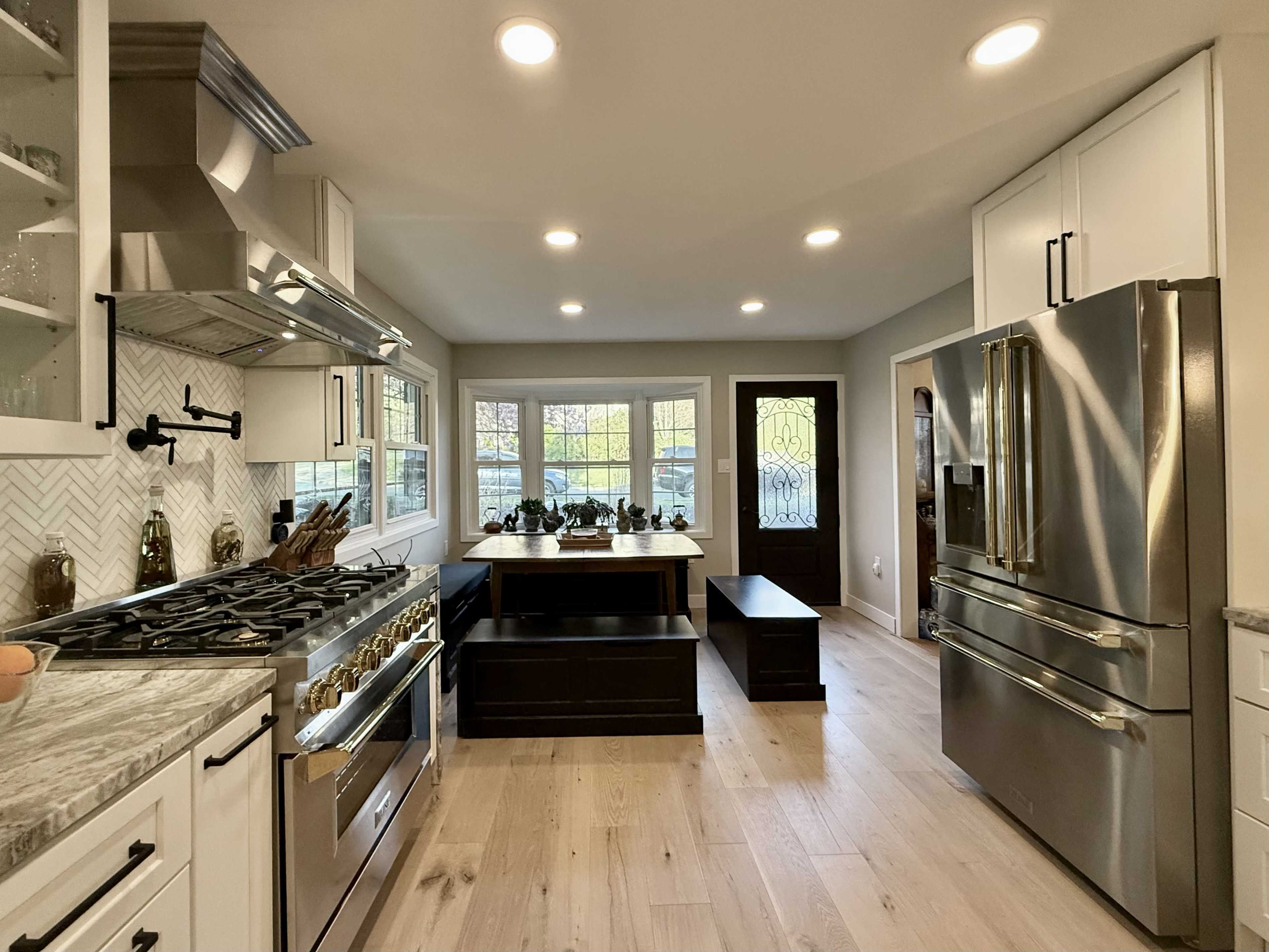 The image shows a modern kitchen featuring stainless steel appliances, a large island with seating, and bright overhead lighting.