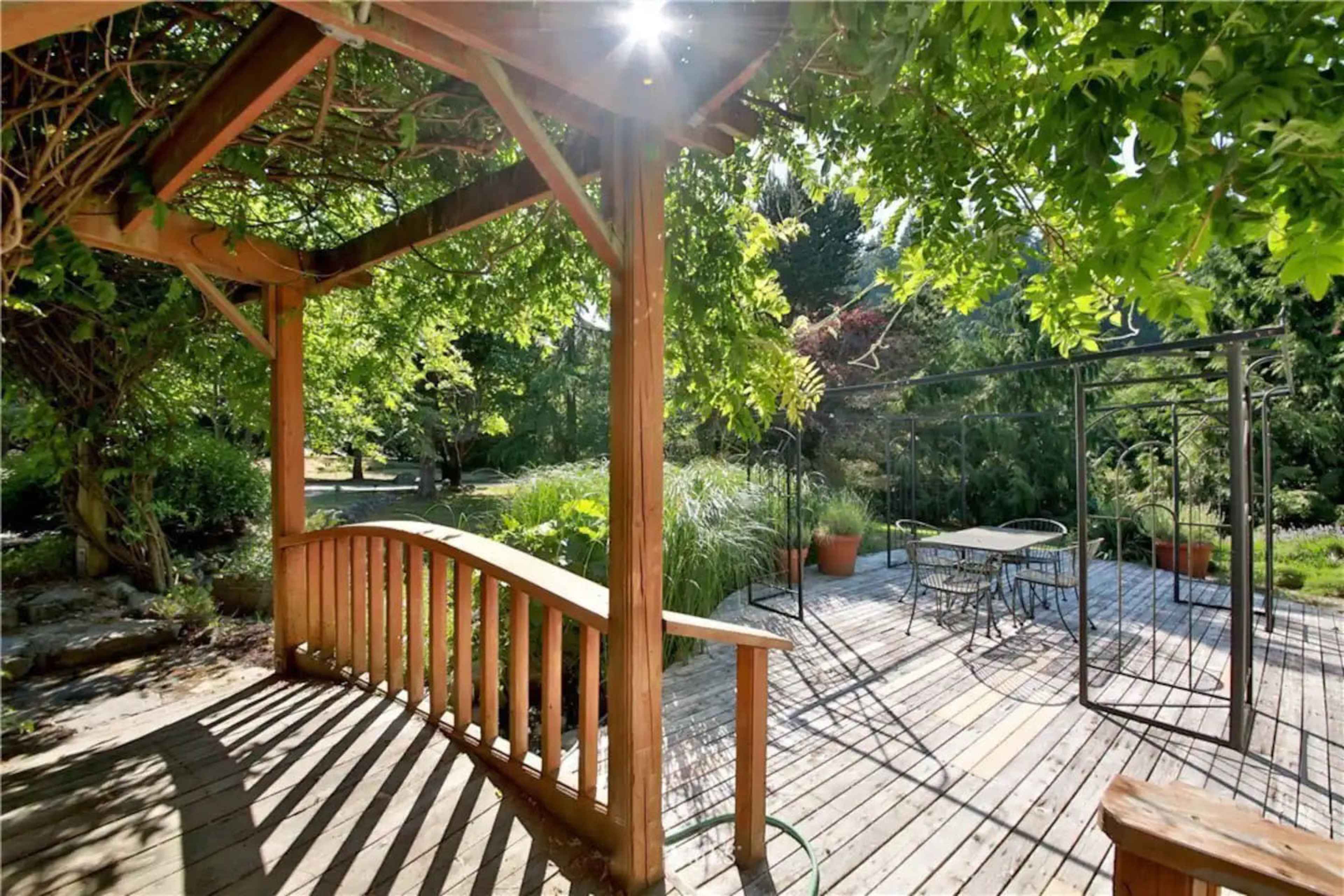 A wooden archway leads to a deck surrounded by lush greenery and outdoor furniture.