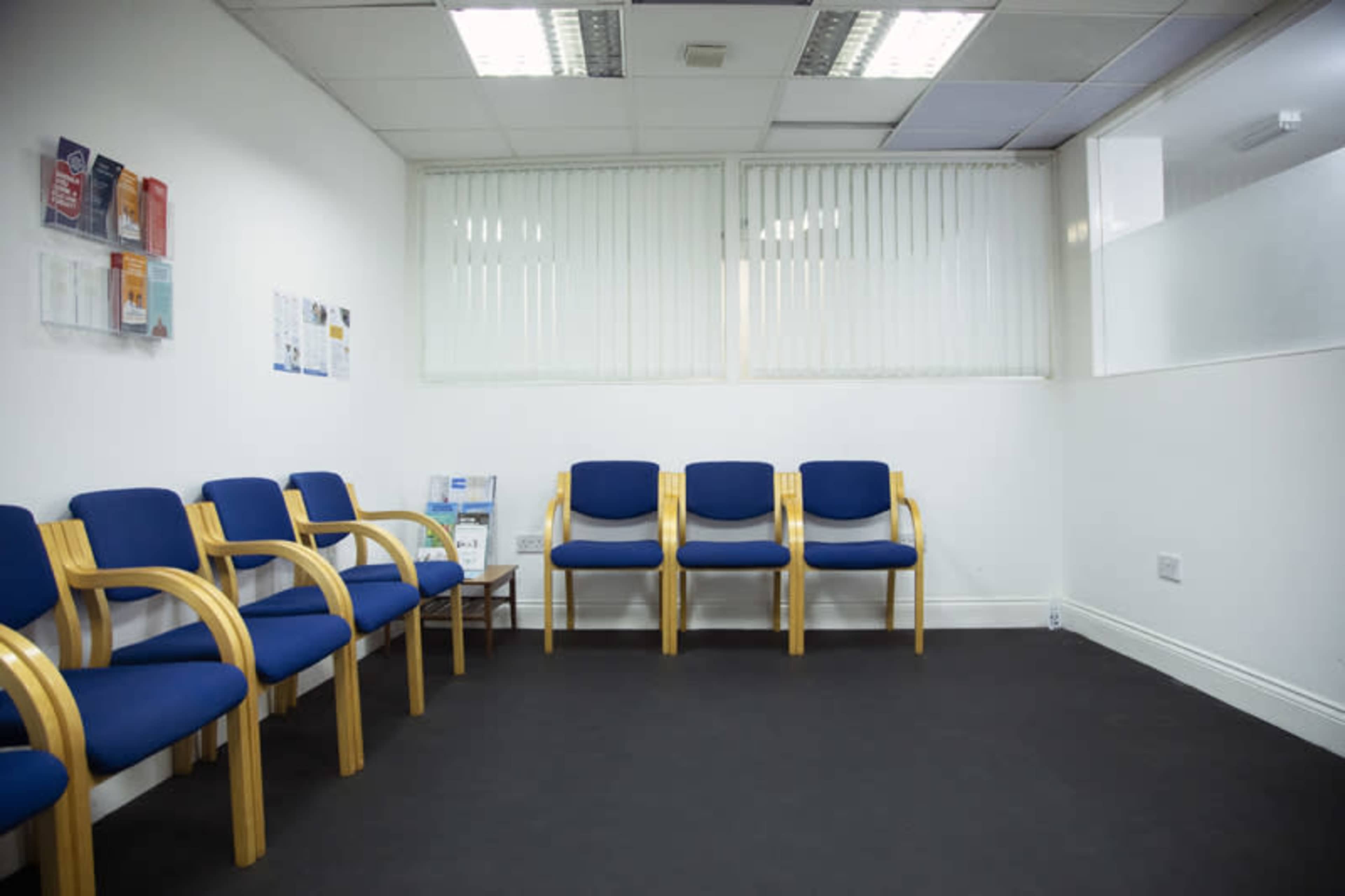 A waiting room with several blue chairs arranged along the wall and a small table with pamphlets in a well-lit space.