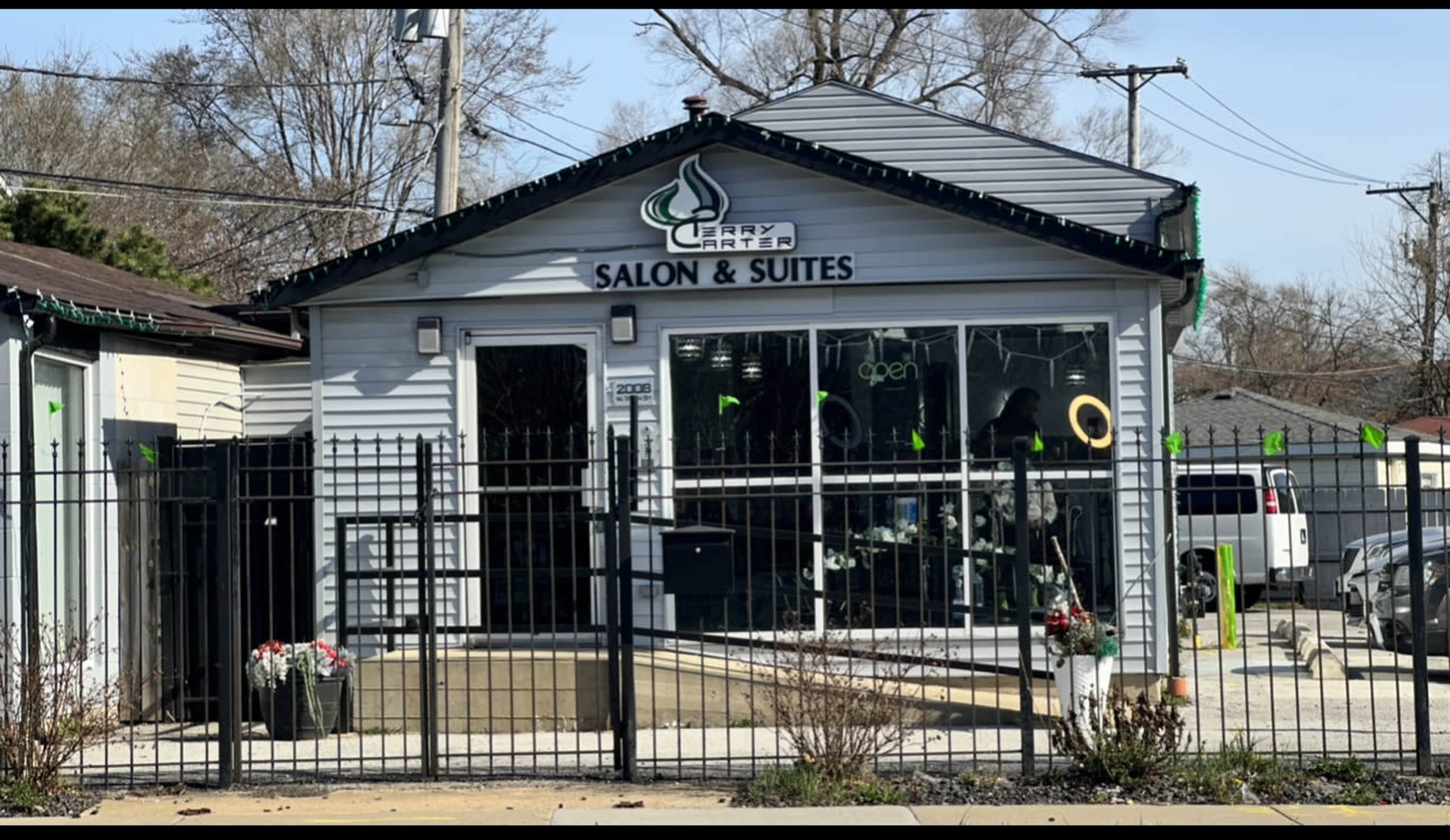 A salon building named "Cerry Tree Salon & Suites," featuring a sign indicating it's open, with a fence and several potted plants in front.