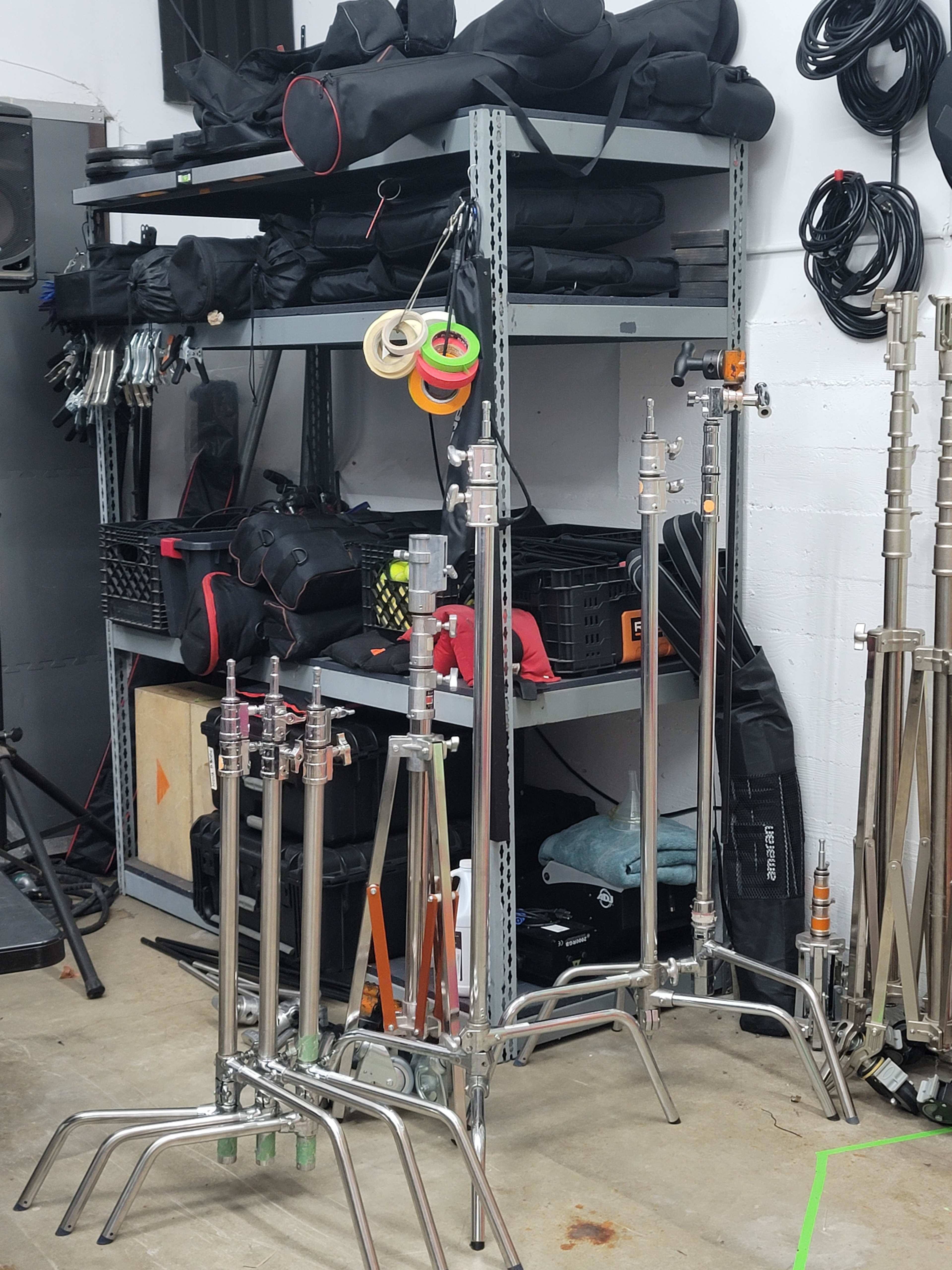 A shelving unit holds various bags and equipment, while several metal stands are arranged on the floor in front of it.