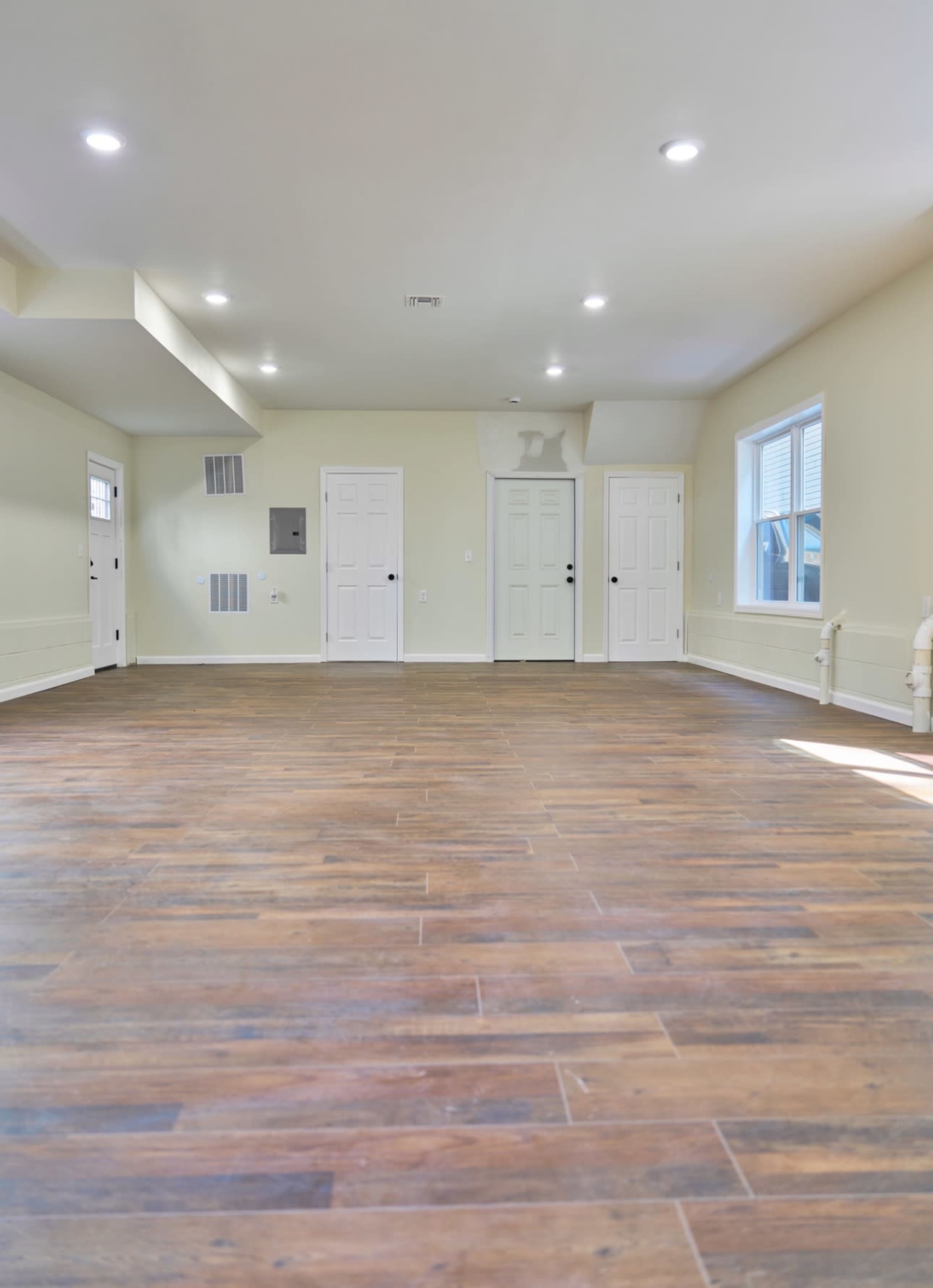 The image shows a spacious, empty room featuring hardwood flooring and multiple doors leading to adjacent areas.