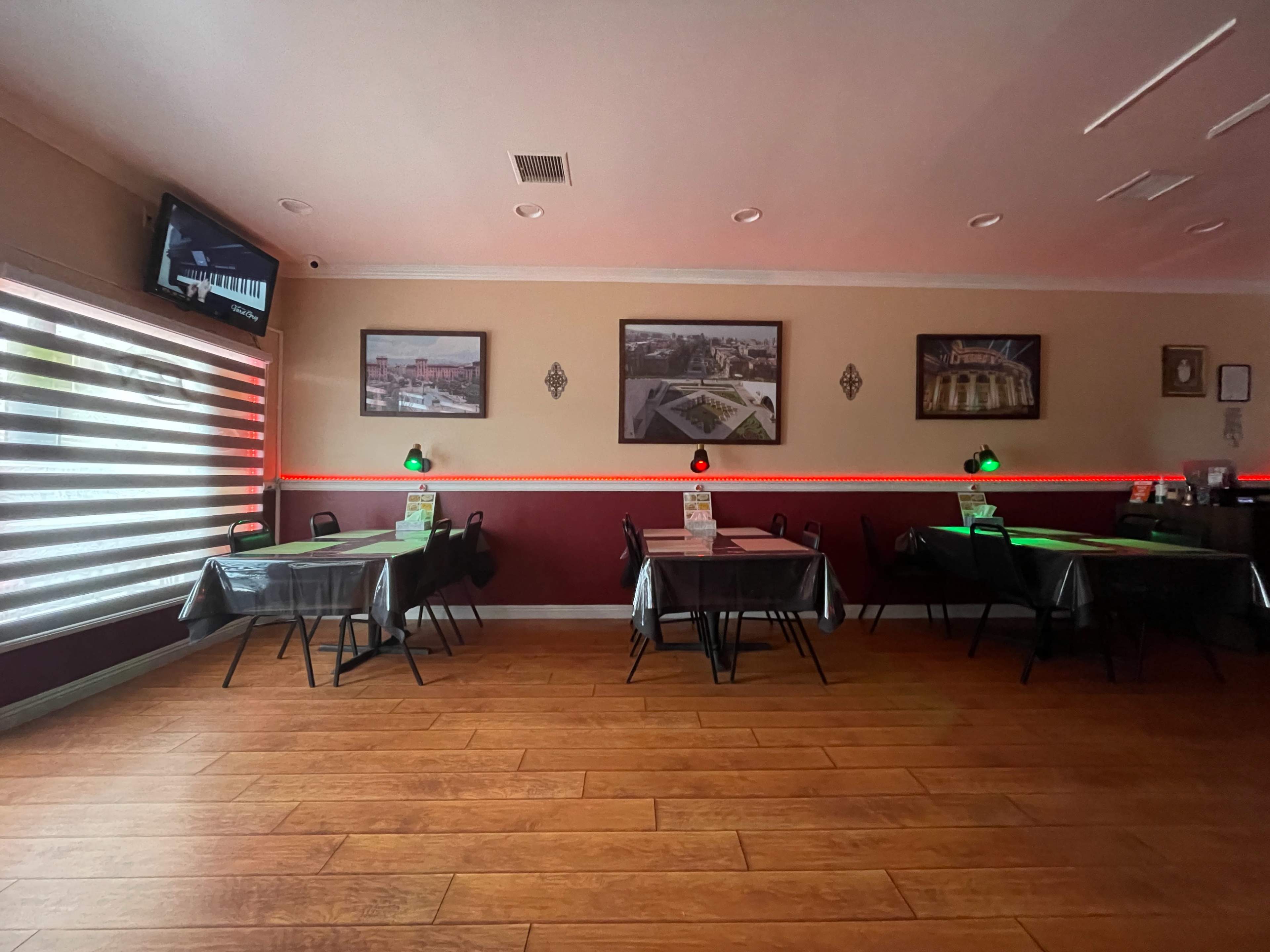 The image shows a dining area of a restaurant with several tables, illuminated by green lamps, and decorated with framed photos on the walls.