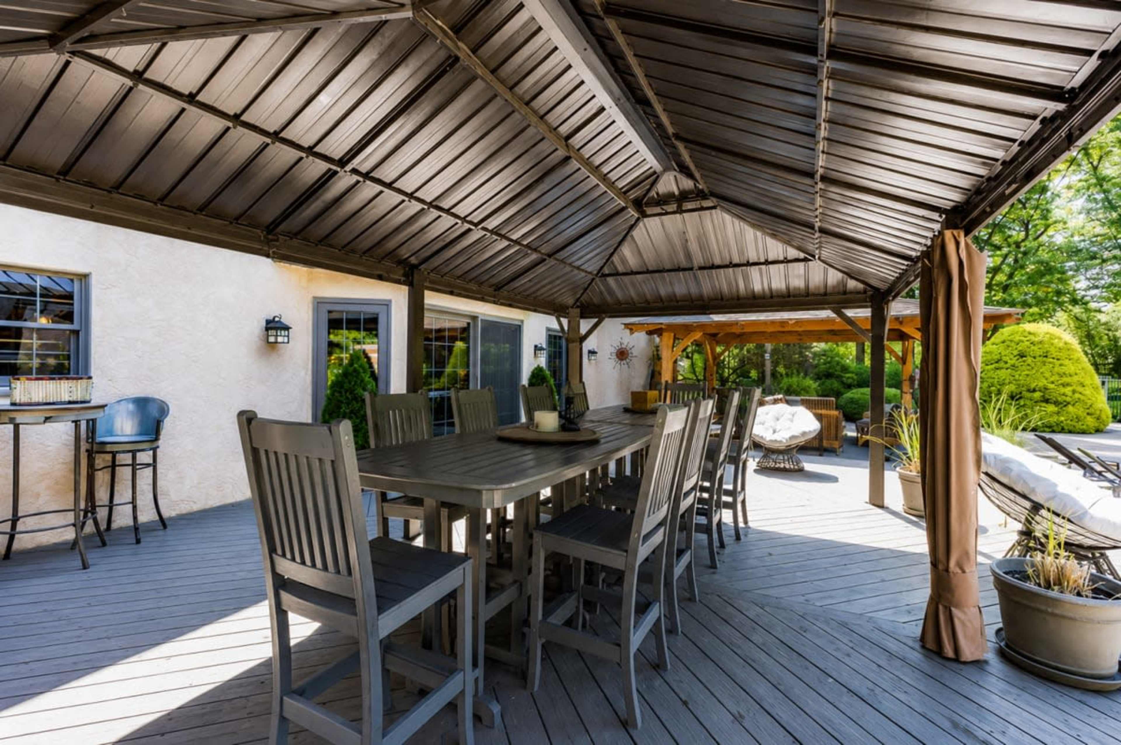 The image shows a spacious outdoor dining area covered by a large gazebo with a wooden table and high-backed chairs.