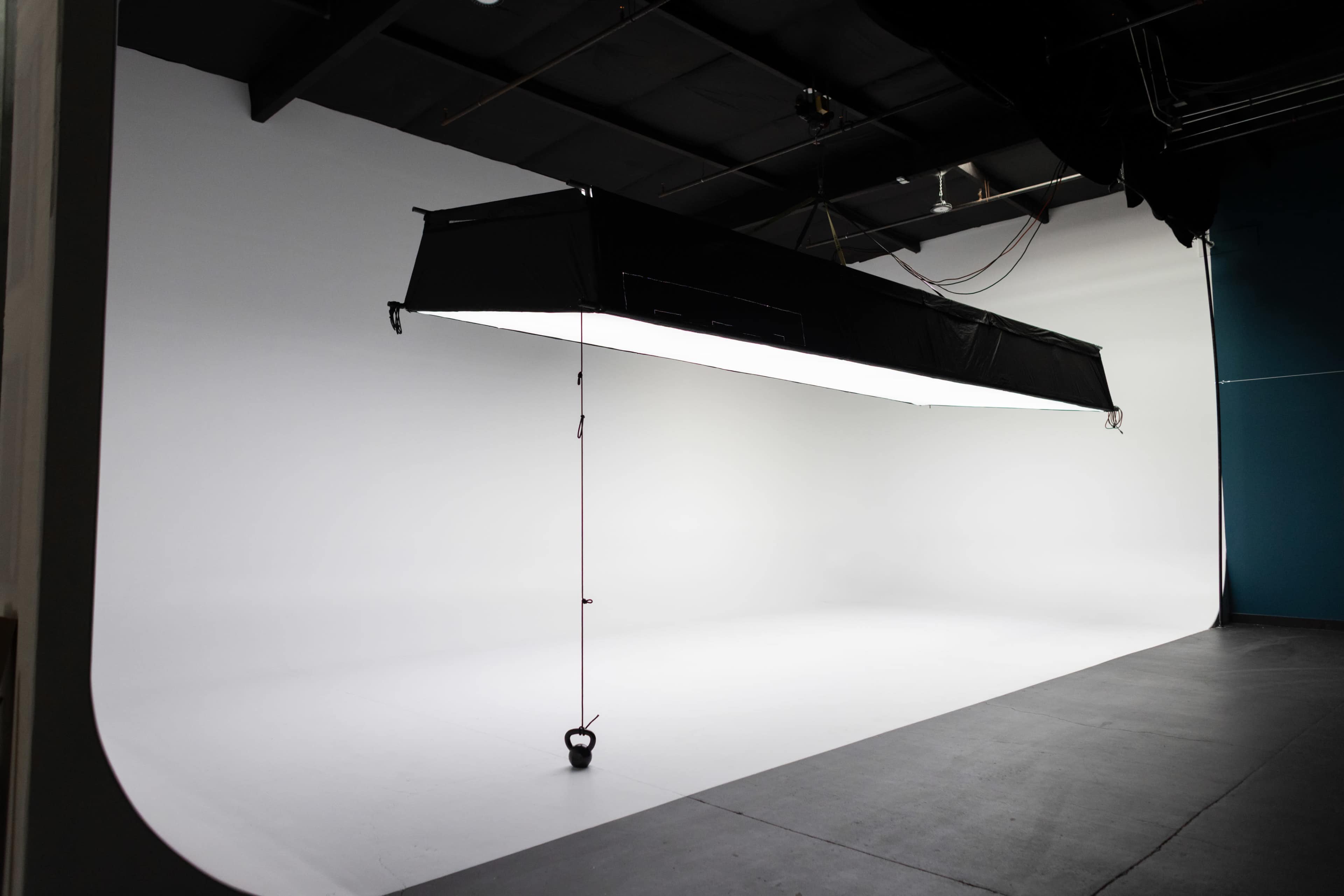 The image shows a photography studio with a large softbox lighting setup hanging over a seamless white backdrop.