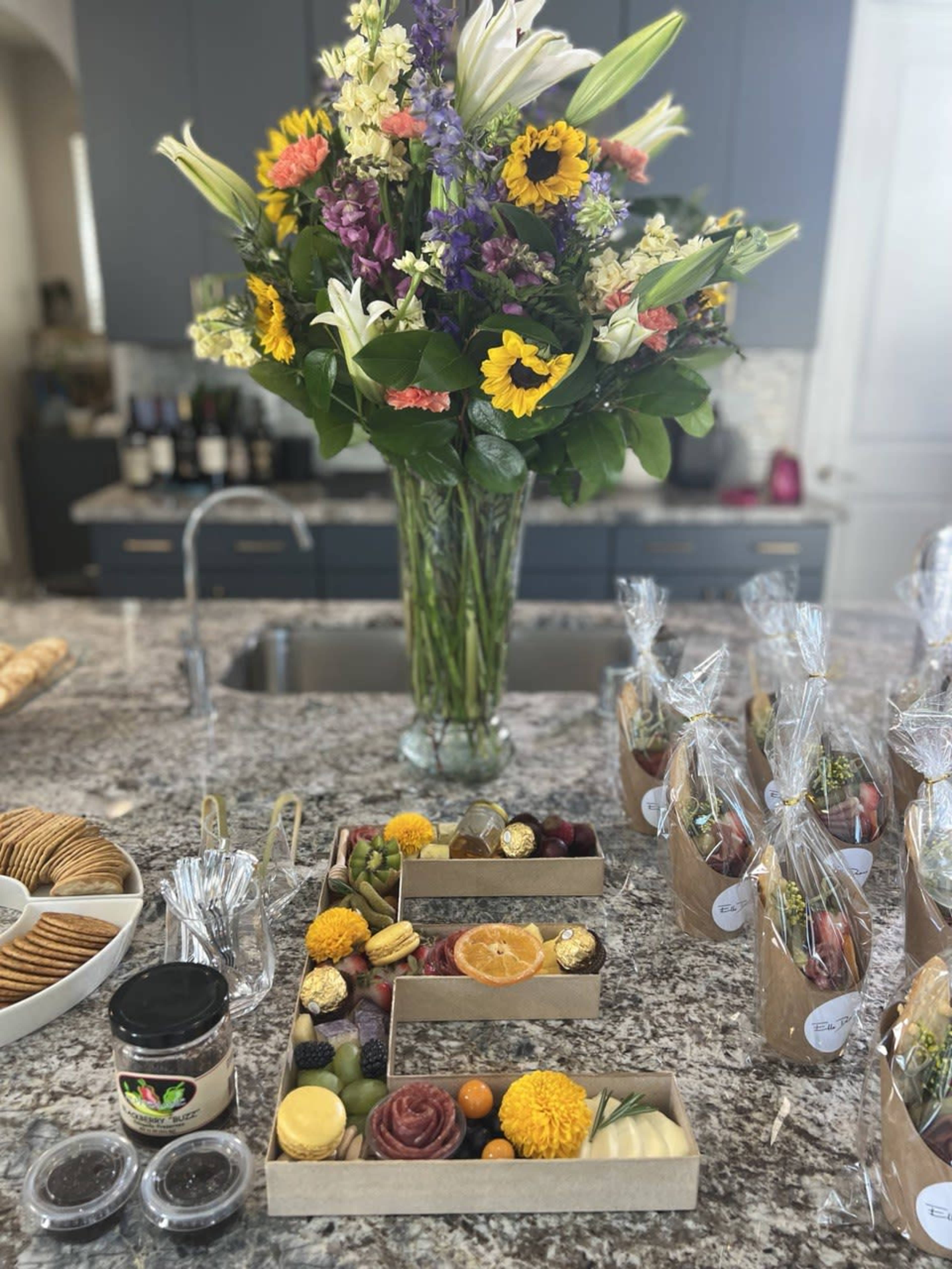 A granite countertop is set with boxes of assorted snacks and a large vase of fresh flowers in the background.
