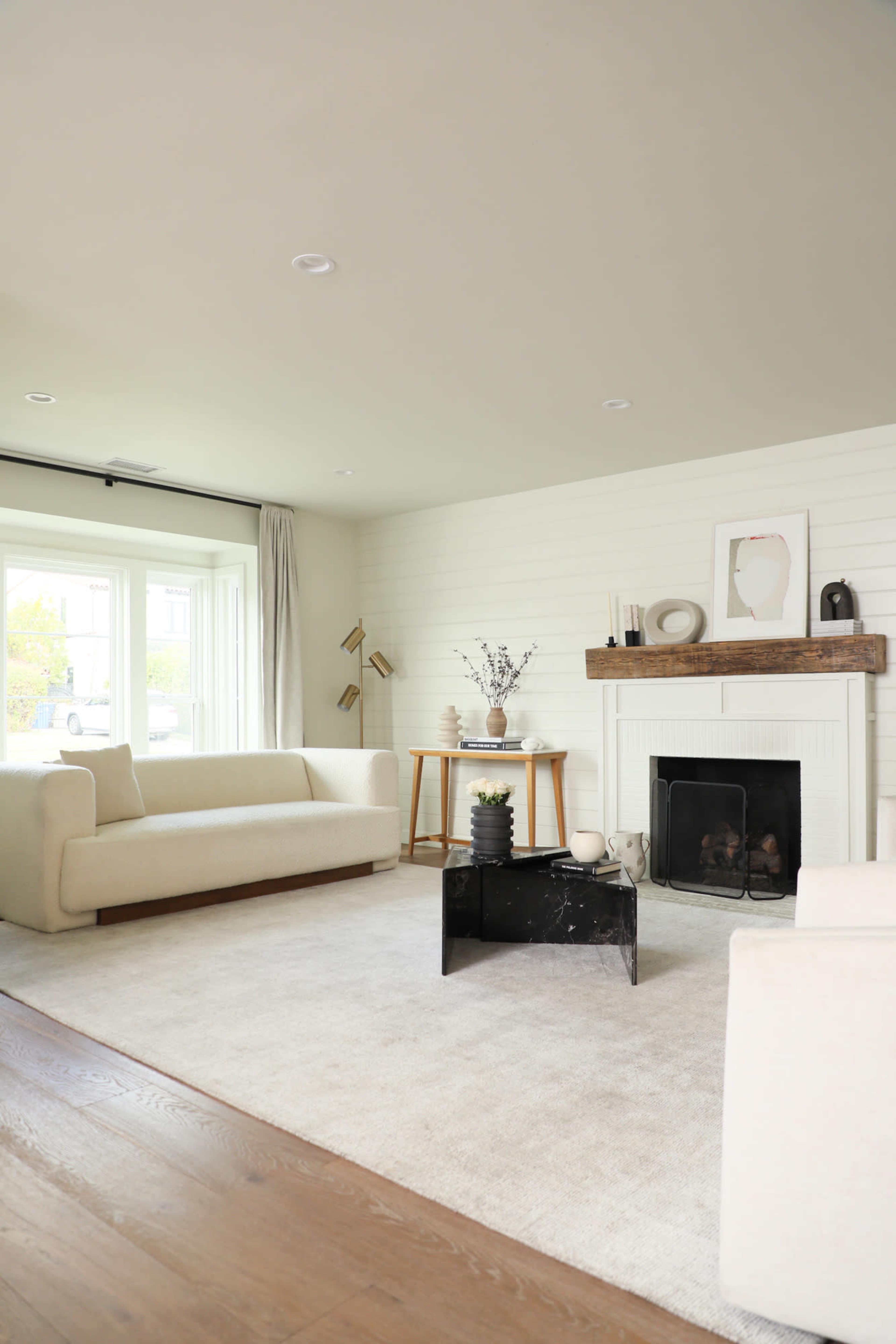 The image shows a minimalist living room with two white sofas, a coffee table, and a fireplace adorned with decorative items.