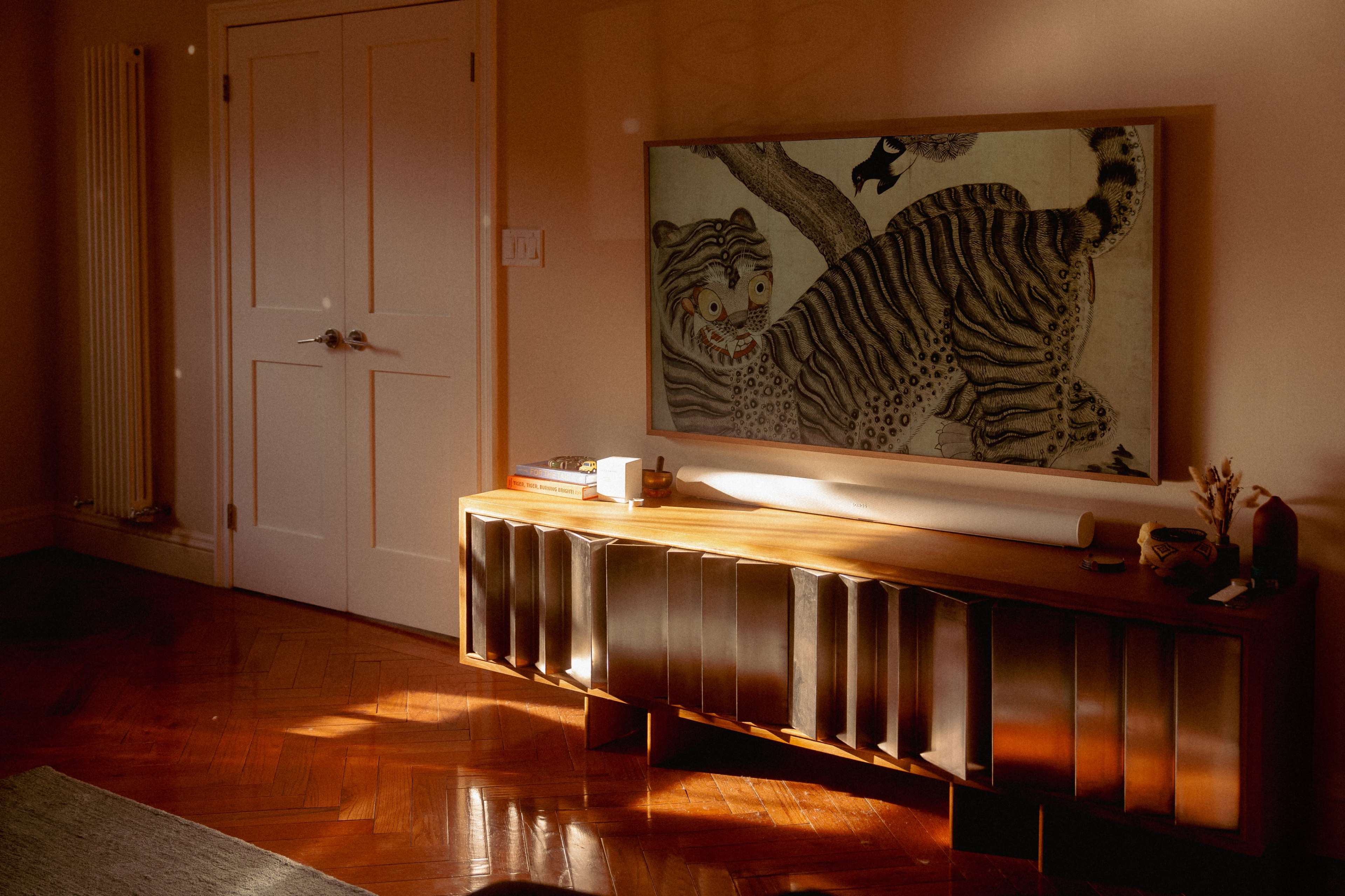 A wooden sideboard with metallic accents displays a framed artwork of a tiger in a softly lit room.