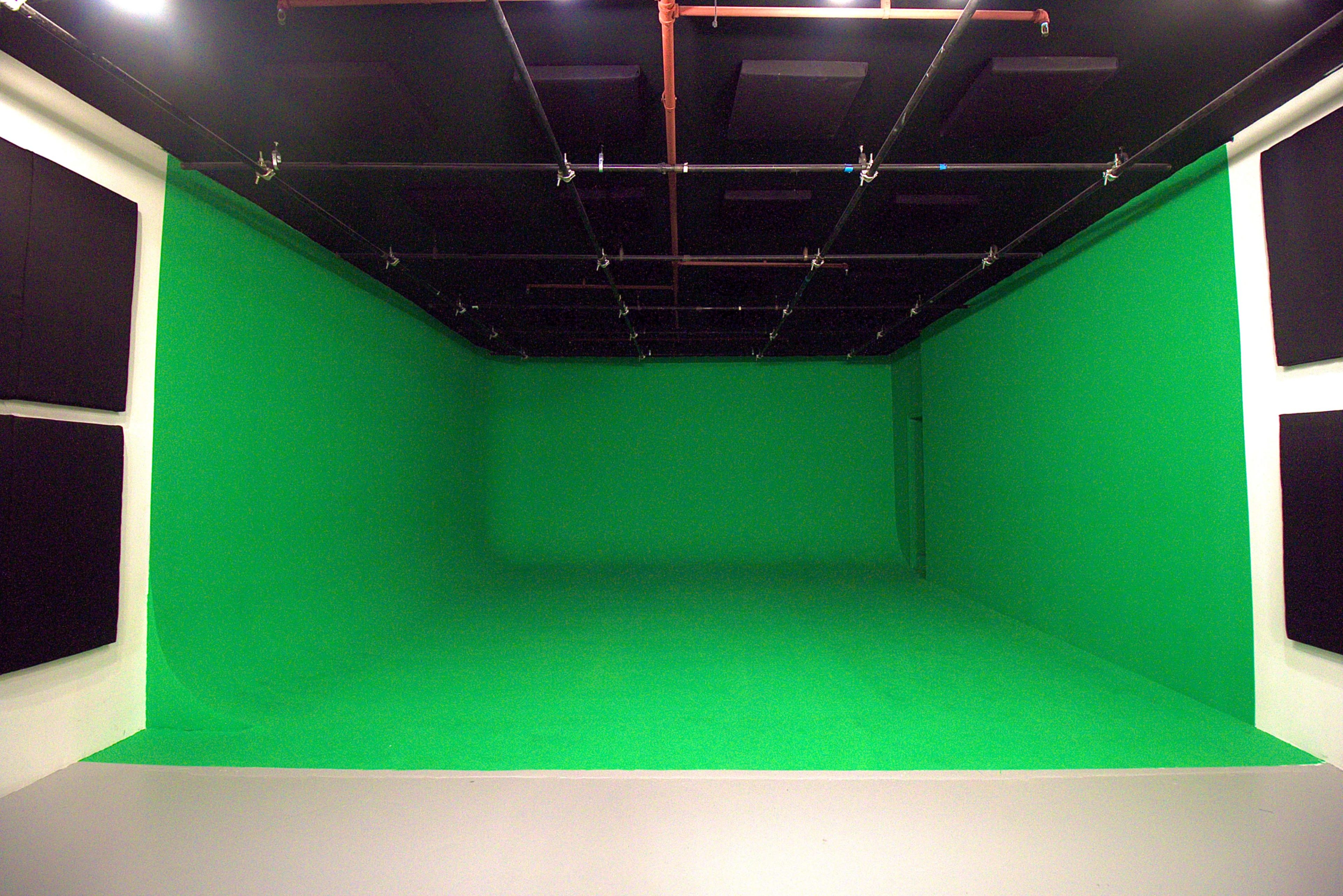 The image shows an empty green screen studio with black soundproofing panels on the walls and a flat gray floor.