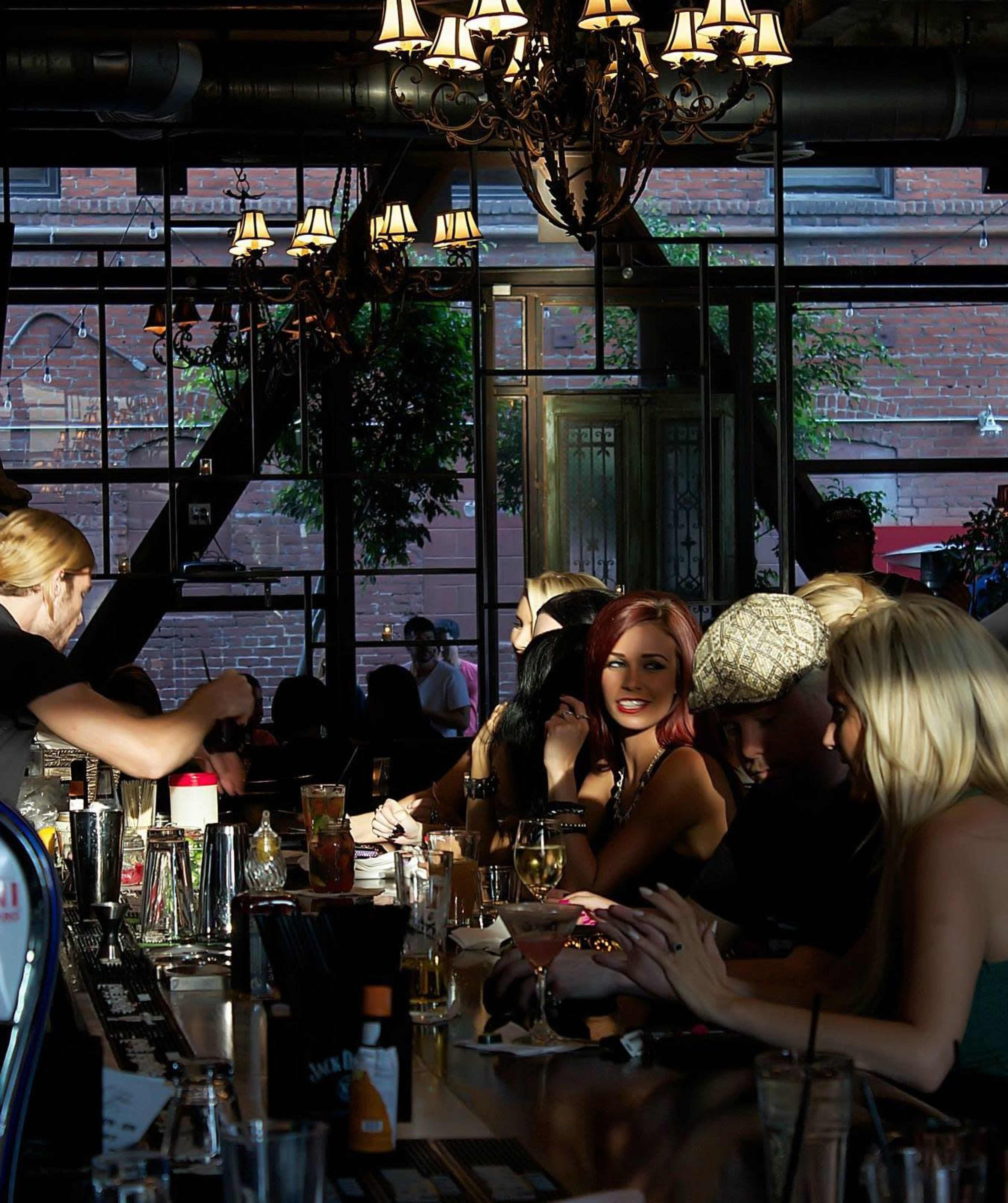 A bartender serves drinks at a lively bar filled with patrons enjoying their evening in a well-lit space.