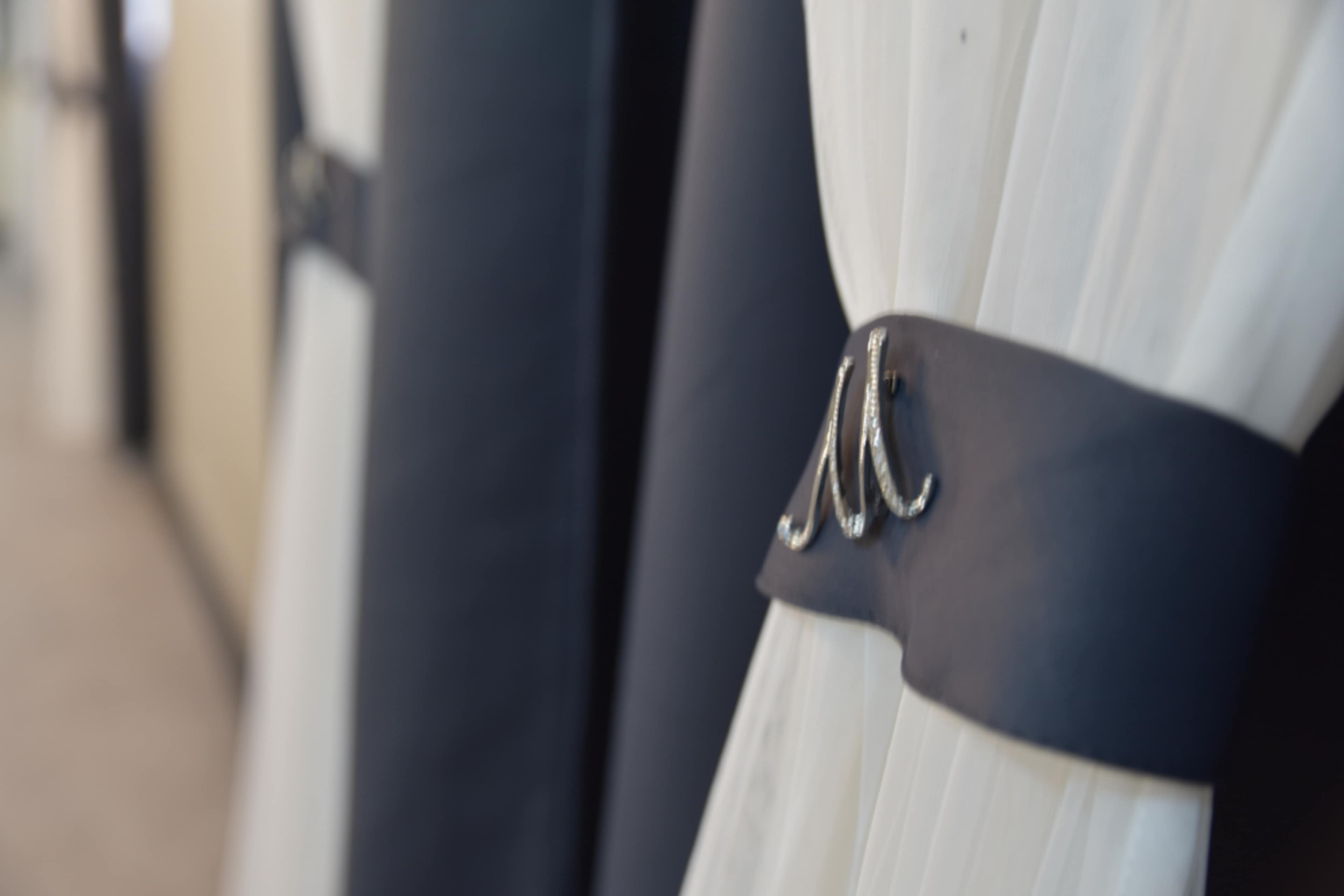 A close-up of a white curtain secured with a dark ribbon featuring a decorative clasp.