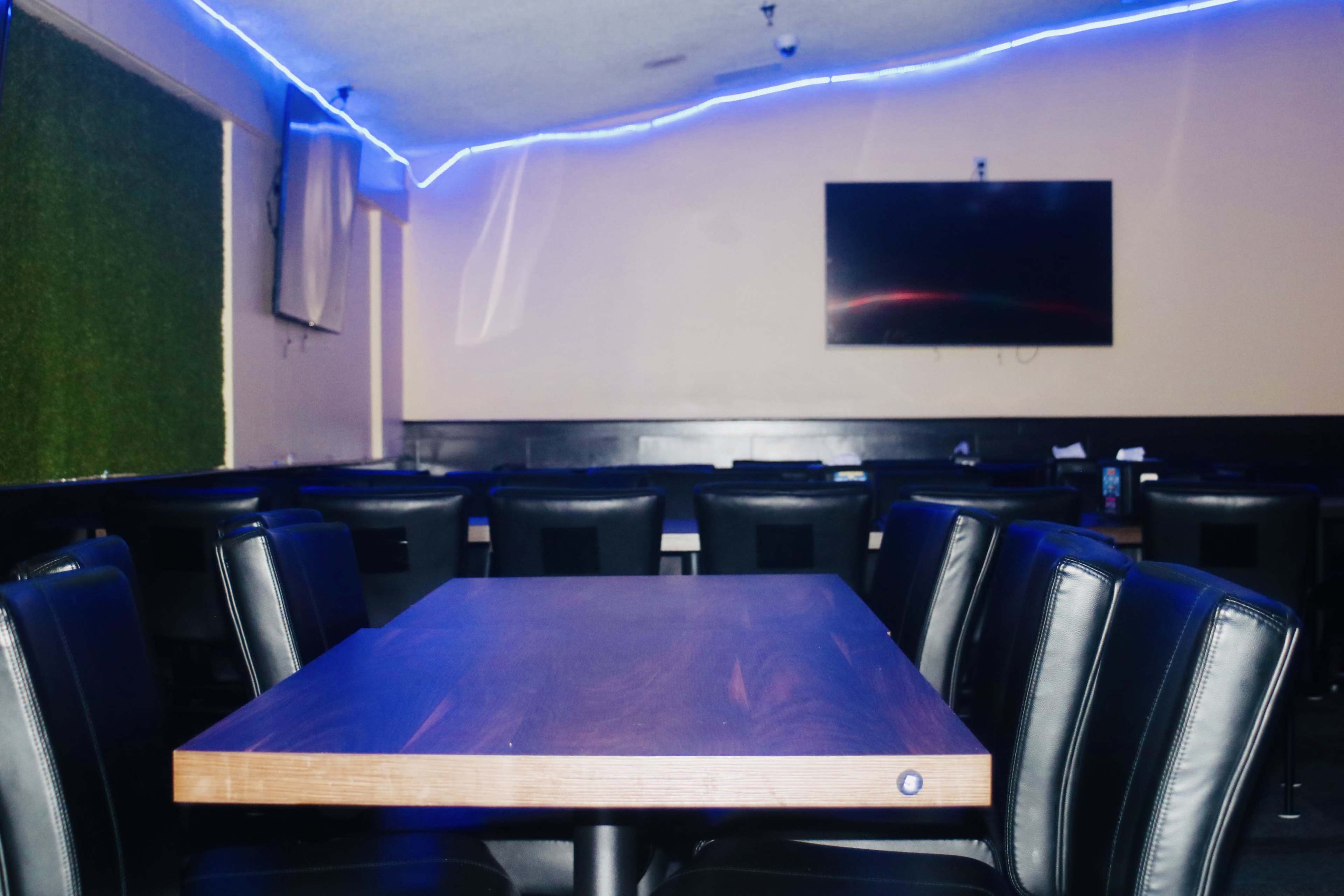 The image shows an empty restaurant interior with black chairs around wooden tables and blue LED lighting along the ceiling.