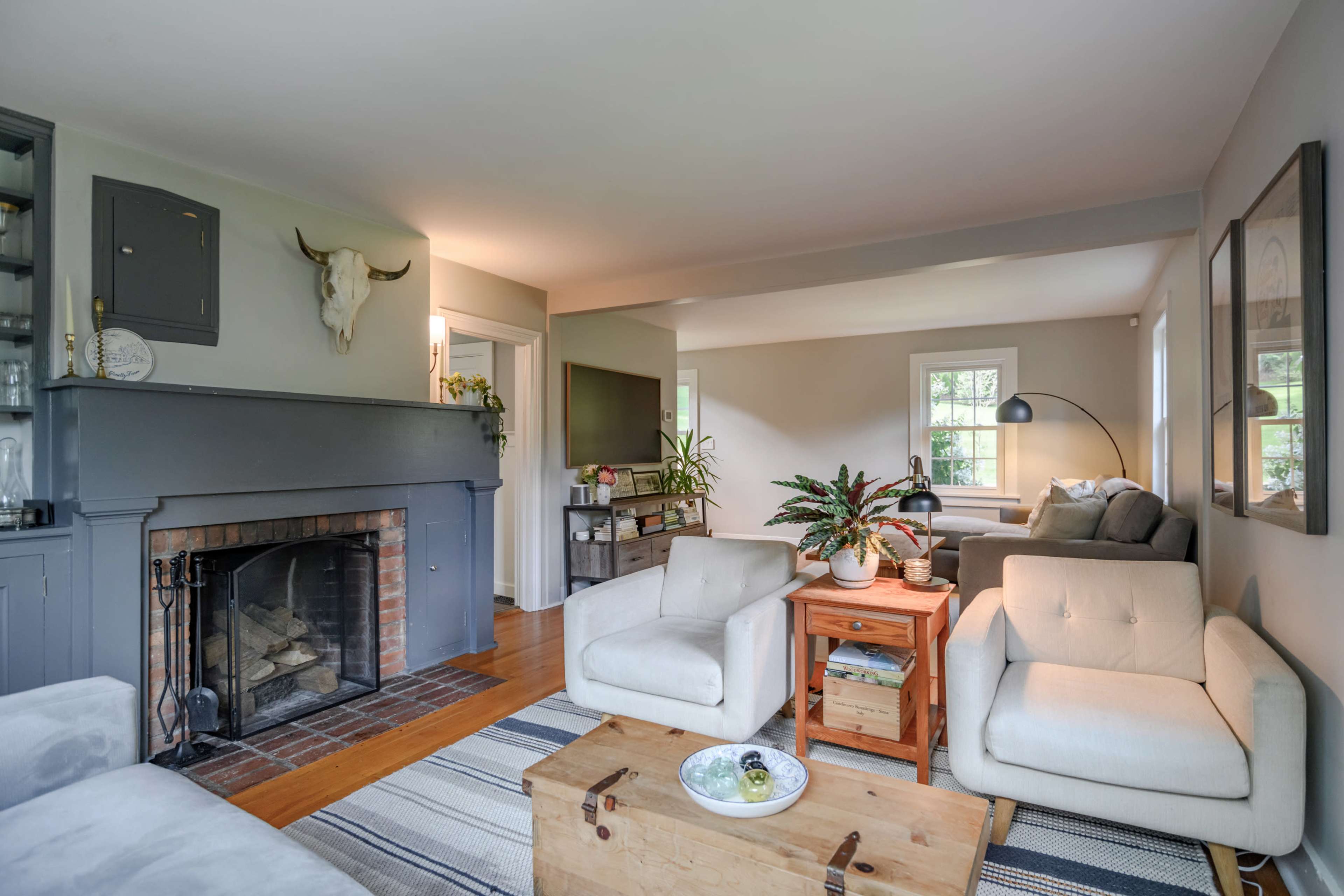 The living room features a fireplace with a decorative mantle, two armchairs, a wooden coffee table, and a television in a softly lit, open layout.