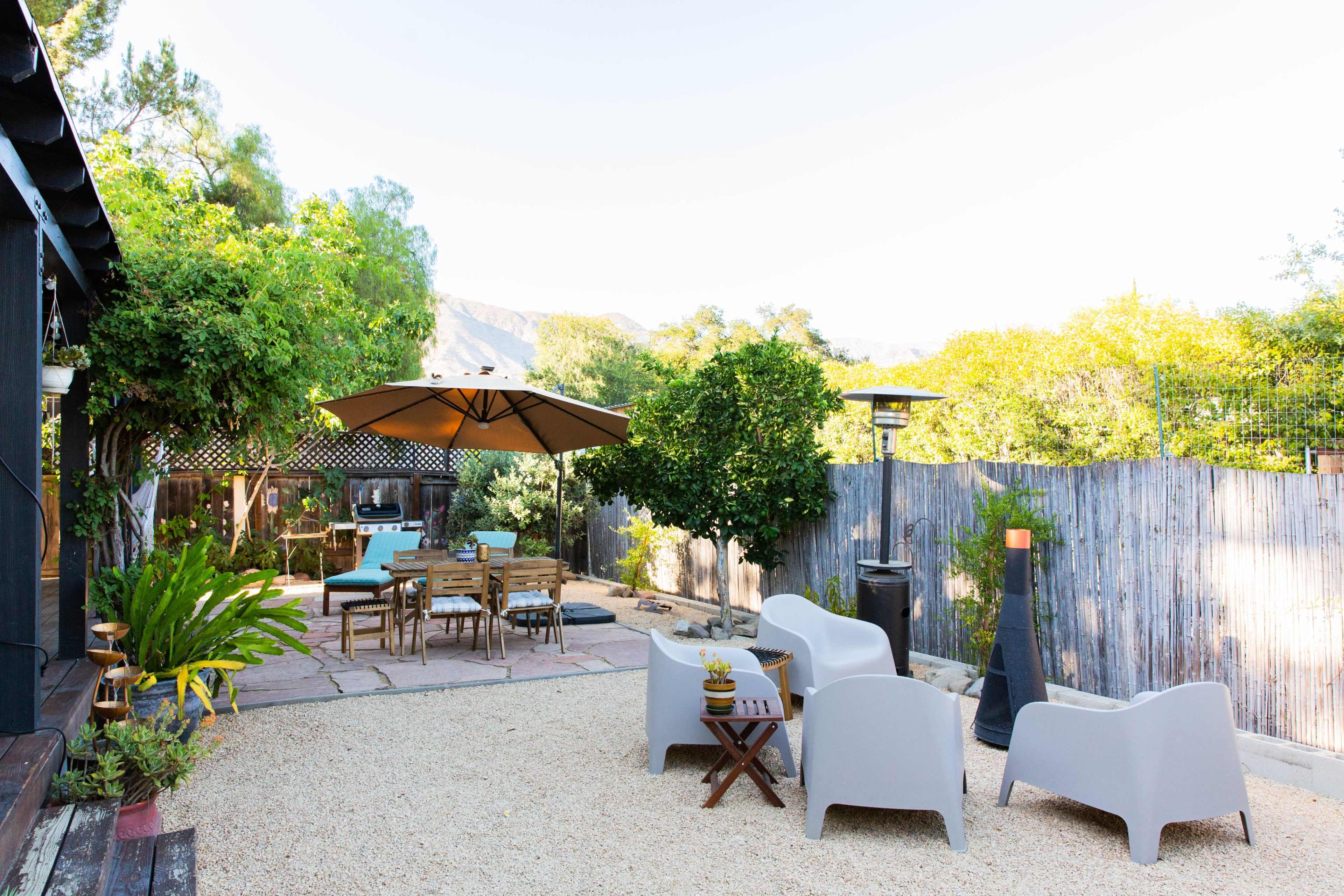 A landscaped outdoor patio features a dining table under an umbrella, adjacent to seating areas with modern chairs.
