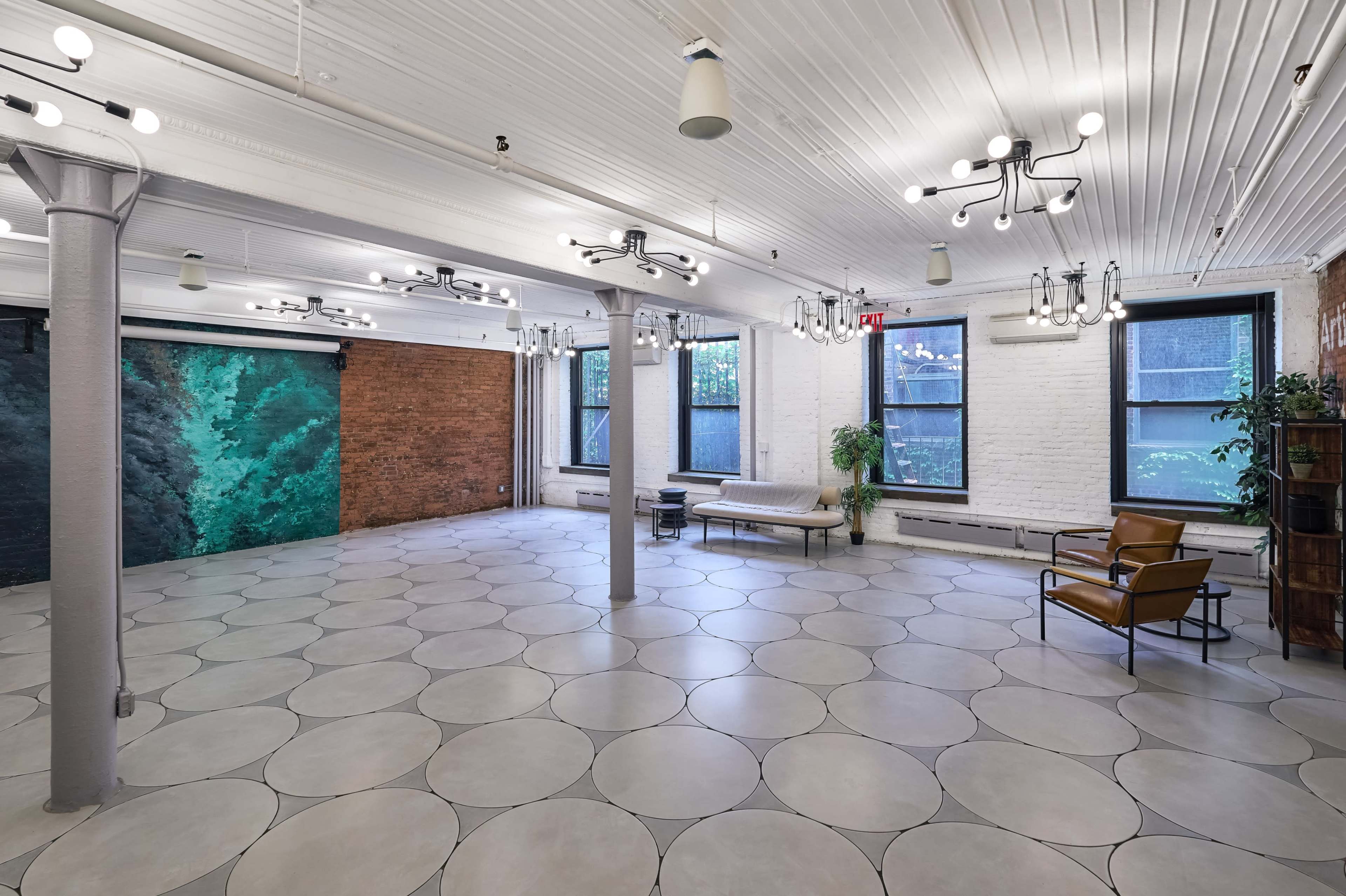 An empty, well-lit room with a polished circular tiled floor, exposed brick walls, and decorative lighting fixtures.