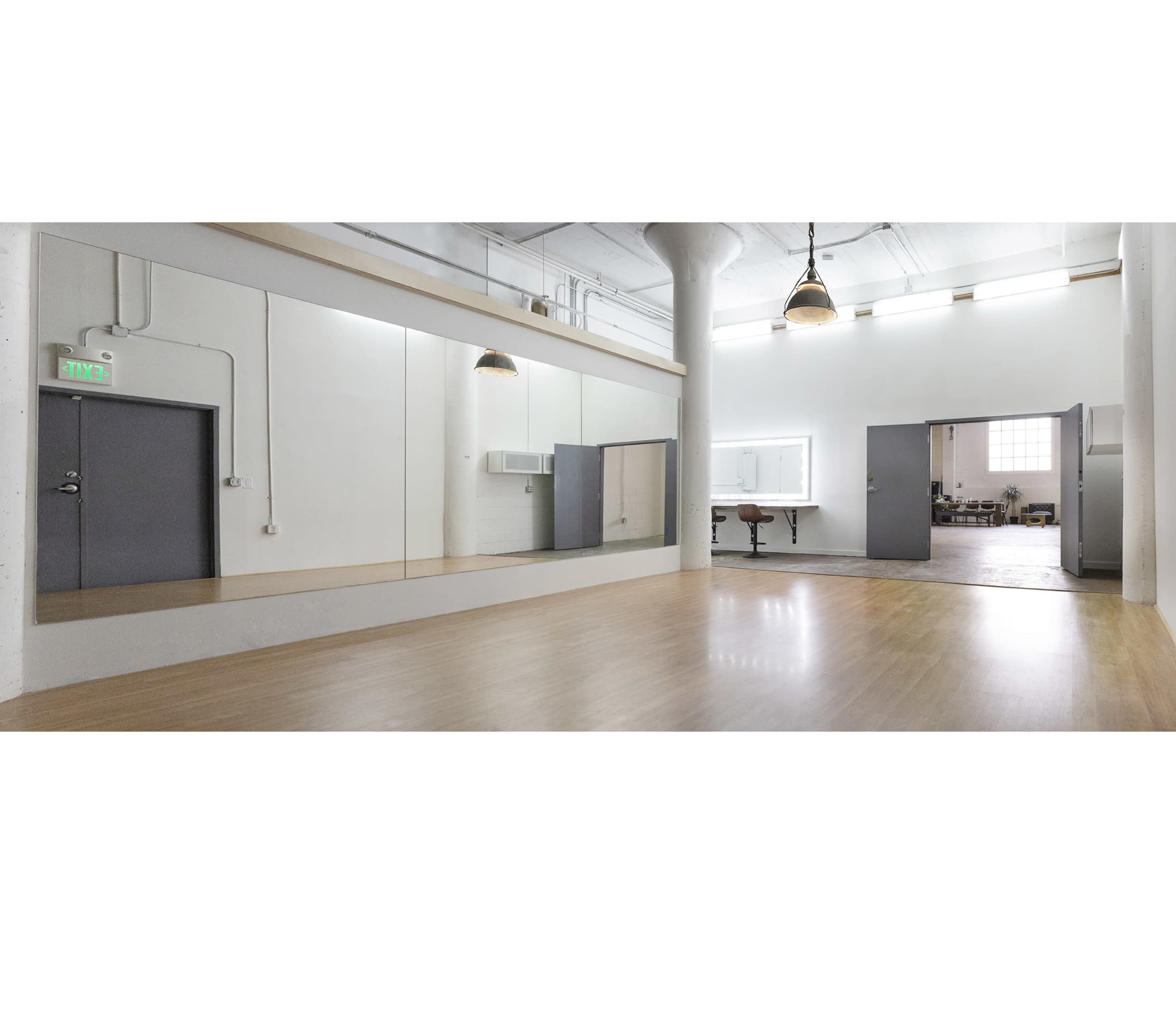 The image depicts a spacious, well-lit studio with polished wooden floors, a large mirror on one wall, and a doorway leading to another area.