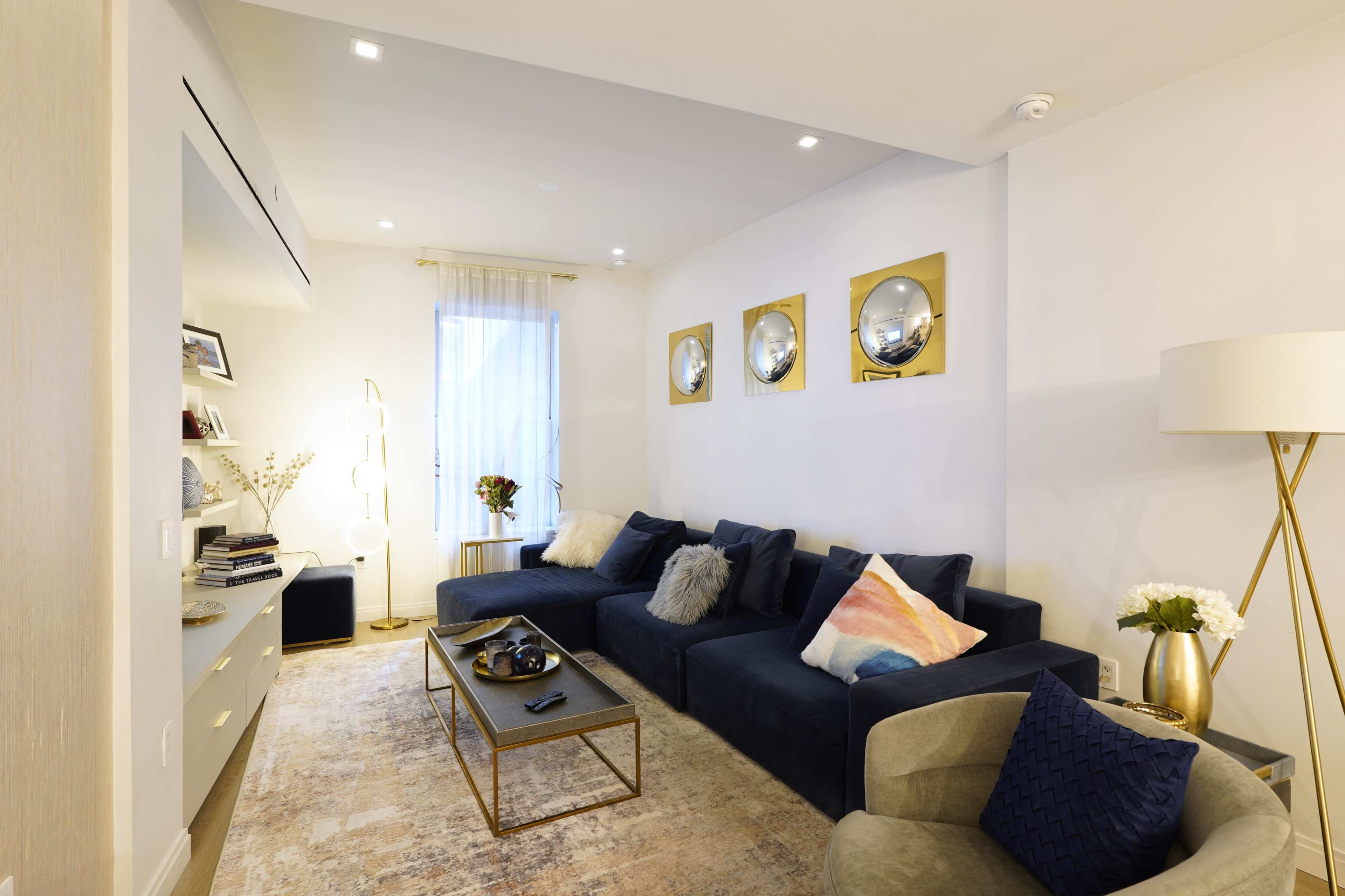 The image shows a modern living room featuring a blue sectional sofa, a light-colored rug, a coffee table, and decorative mirrors on the wall.