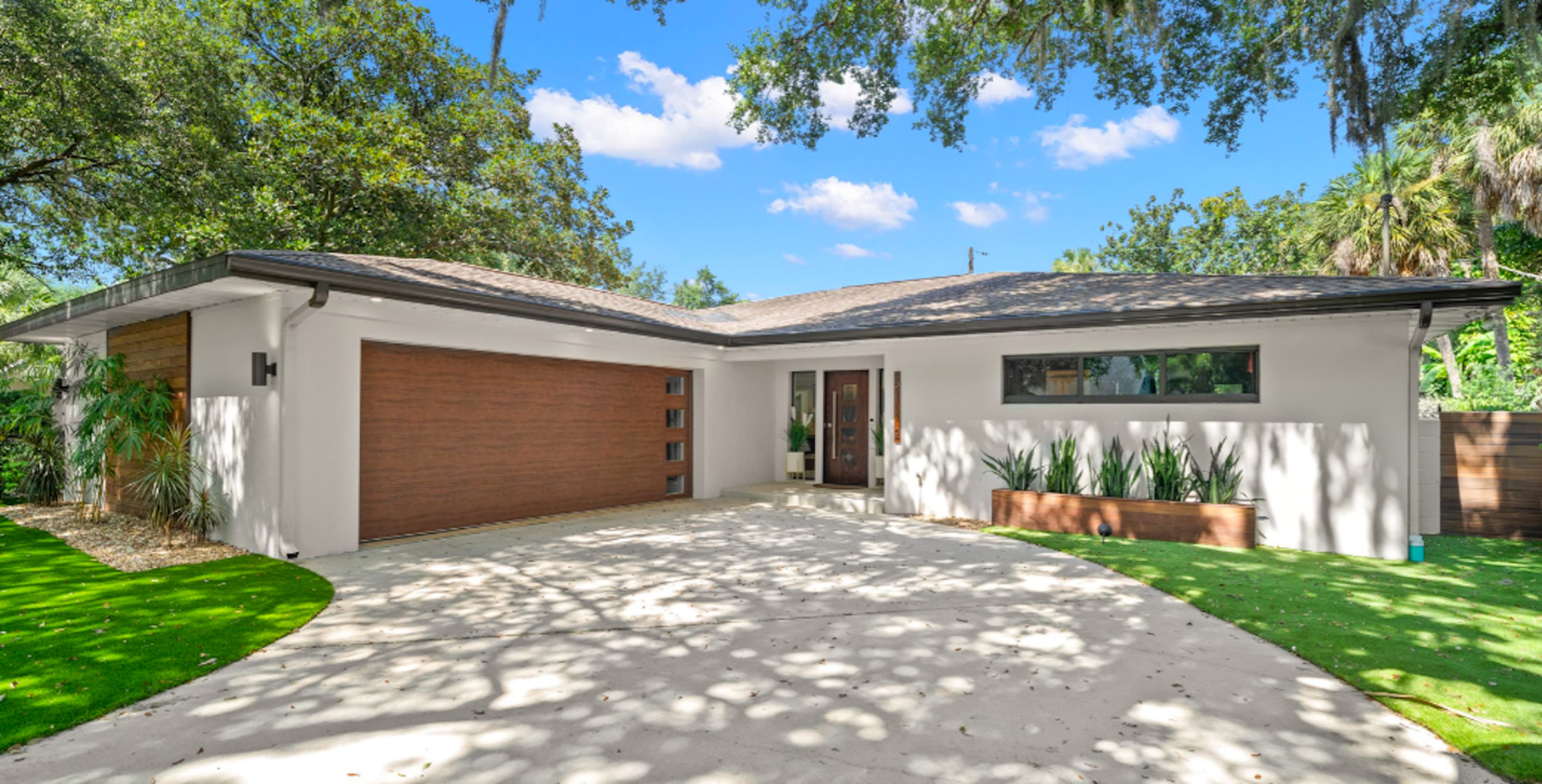 A modern house with a brown garage door, a landscaped front yard, and a circular driveway surrounded by greenery.