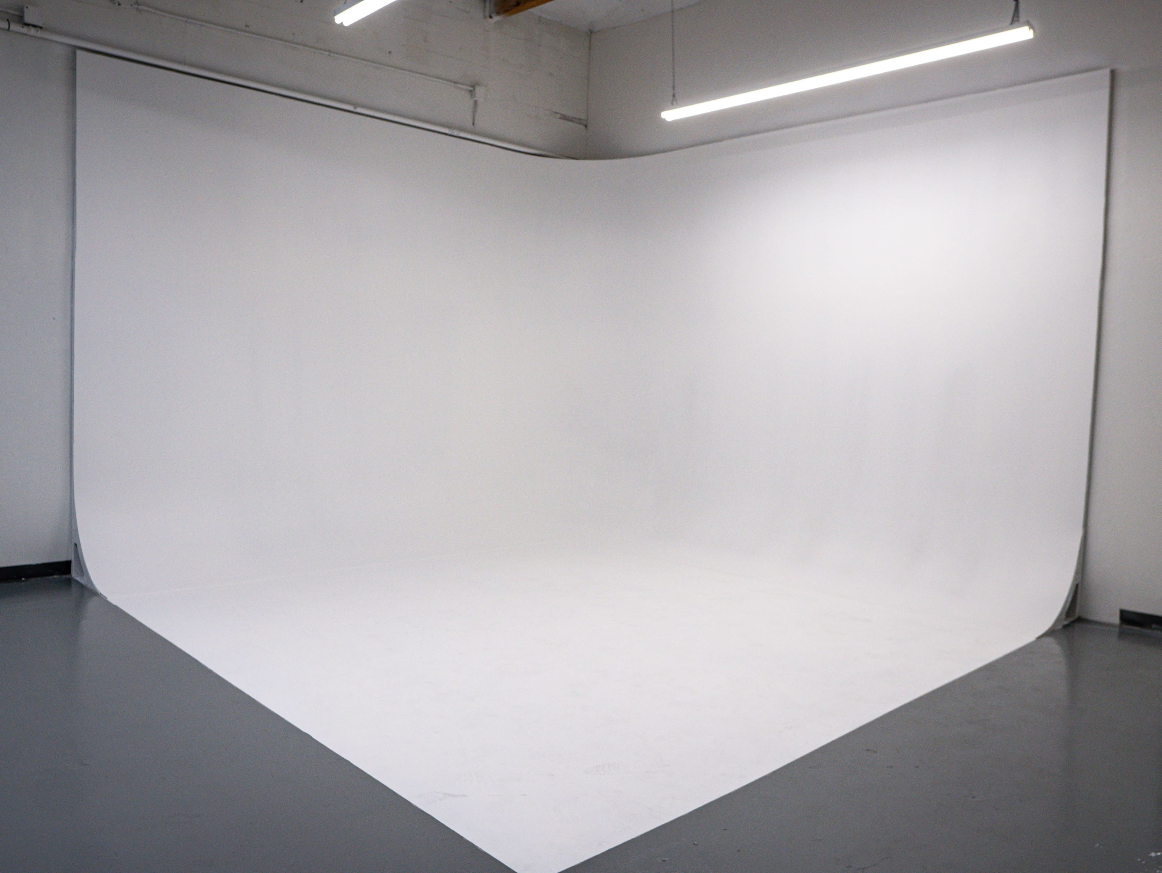The image shows a minimalist photo studio with a curved white background and gray flooring.