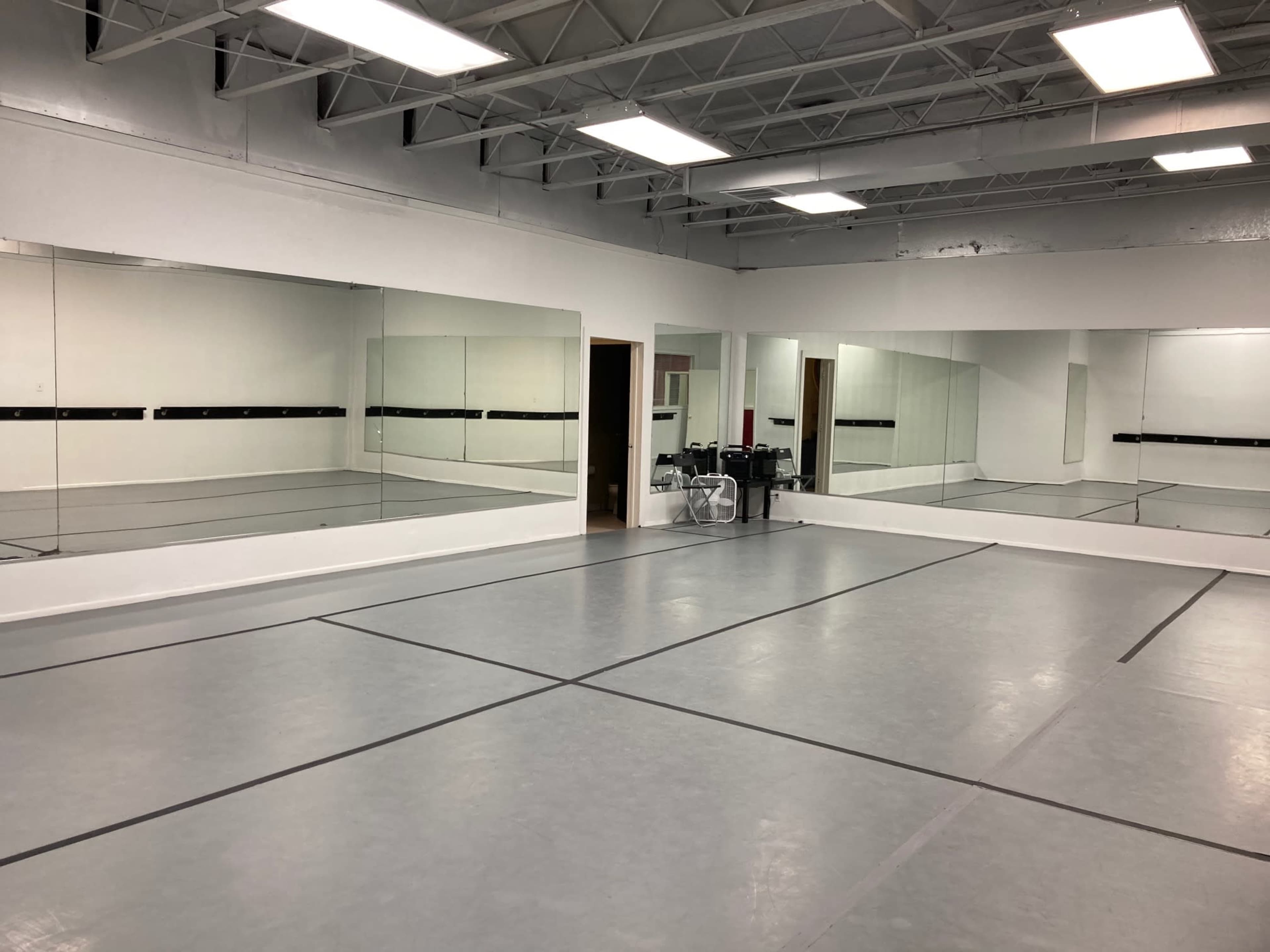 A spacious dance studio with mirrored walls and a gray flooring marked by black lines.