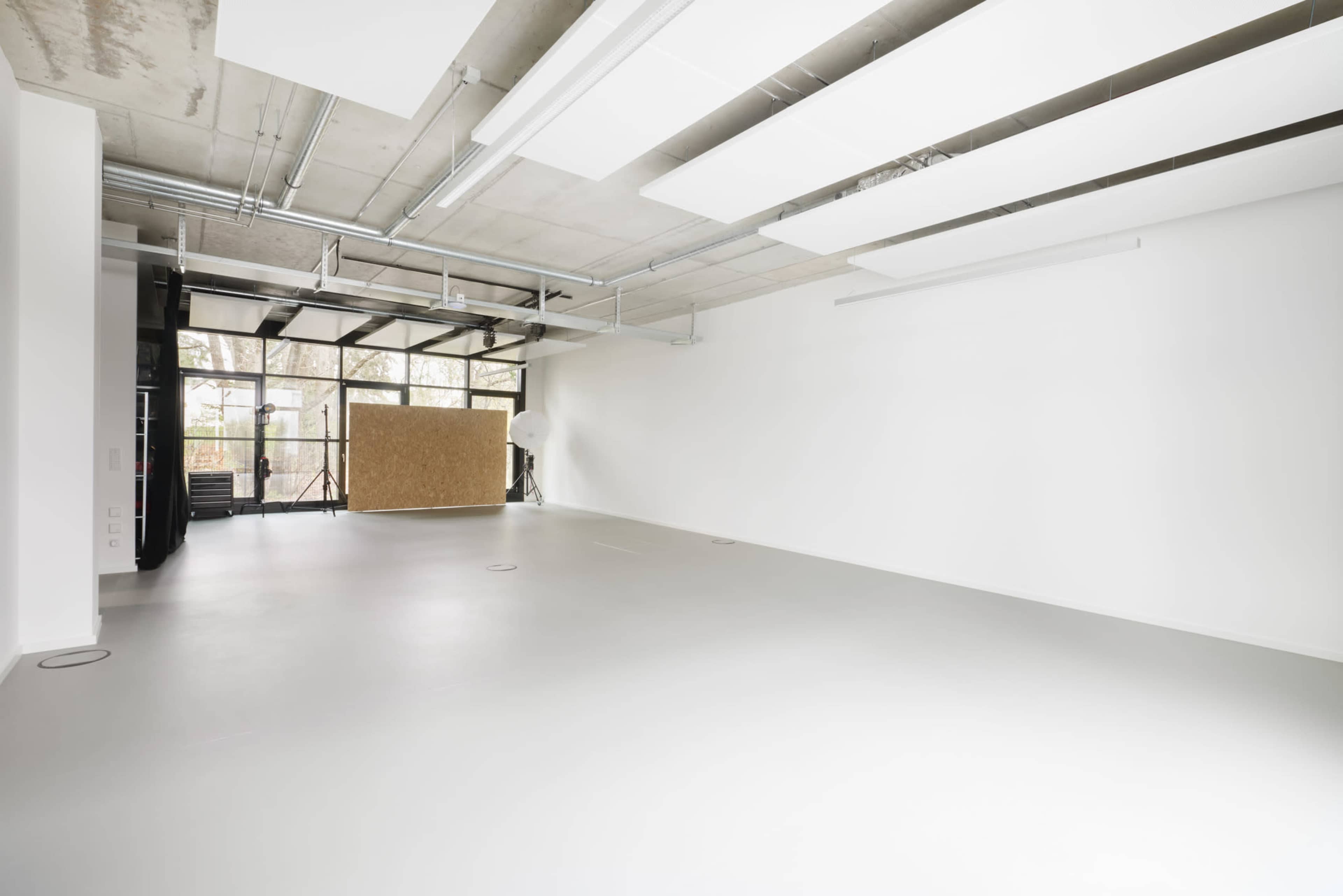 A spacious, empty room with concrete ceilings and large windows letting in natural light.