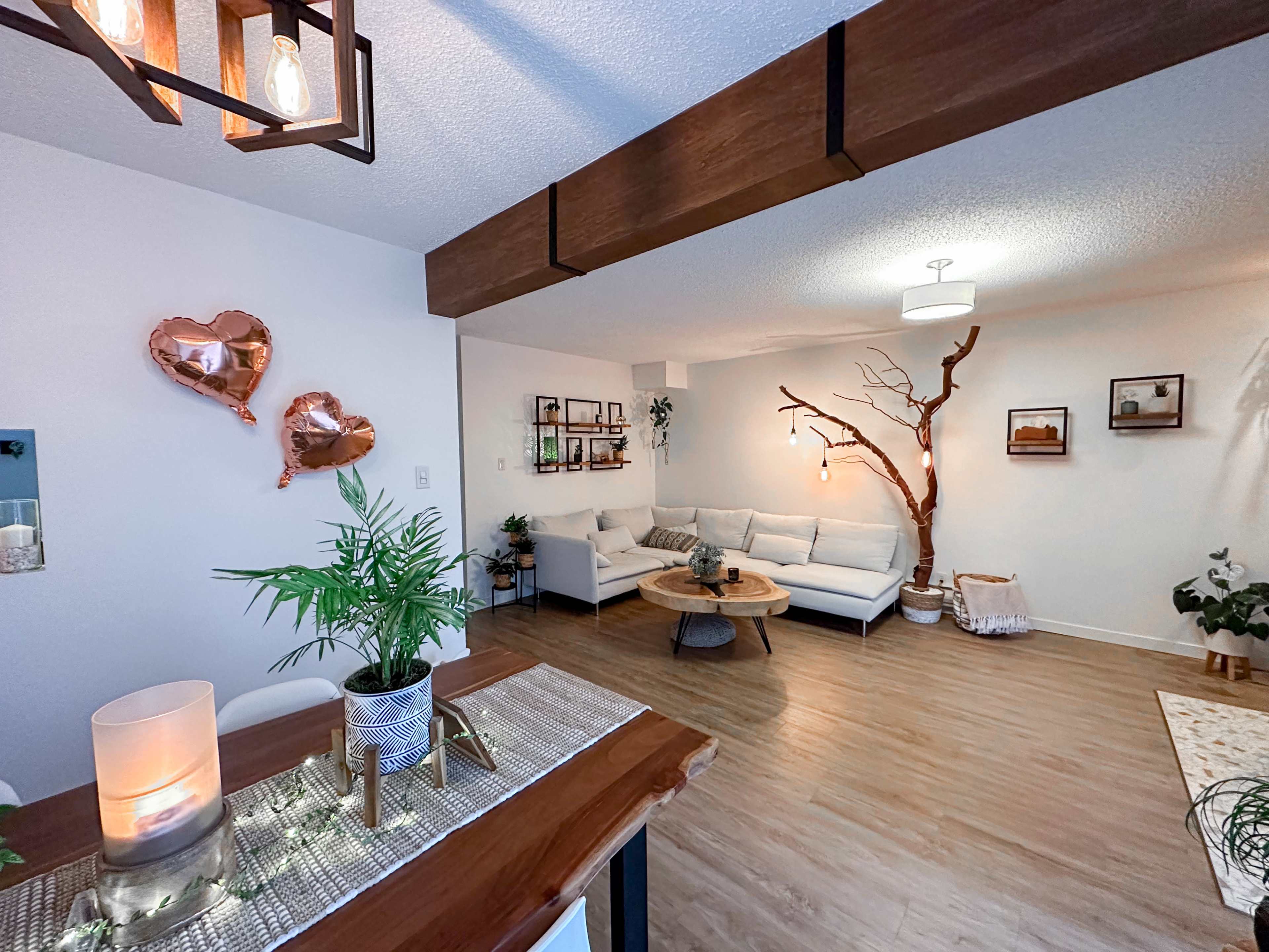 A modern living room with a white sectional sofa, a coffee table, and decorative elements including a tree branch and heart-shaped balloons.