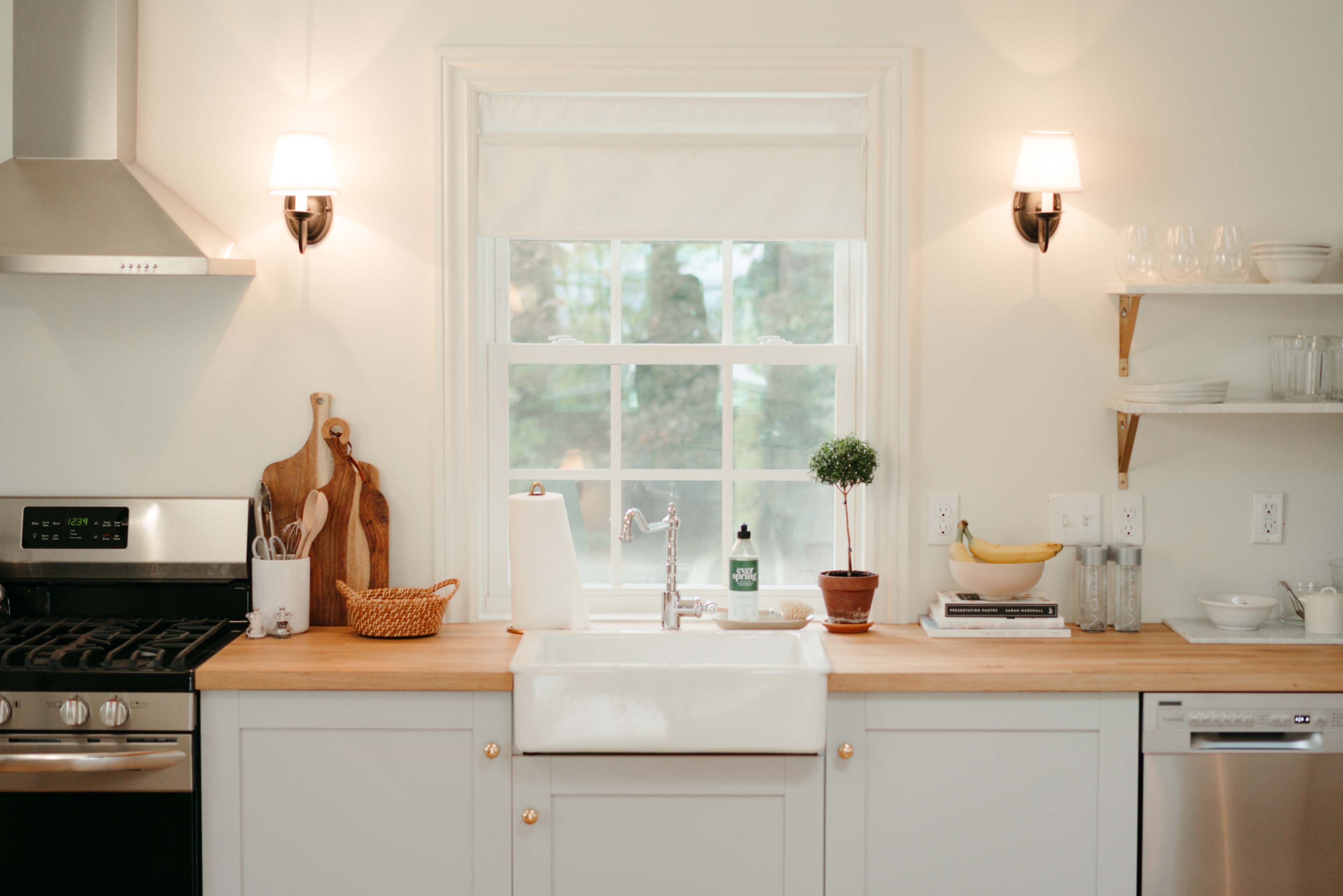 A modern kitchen features a farmhouse sink, wood countertops, and large windows with natural light illuminating the space.