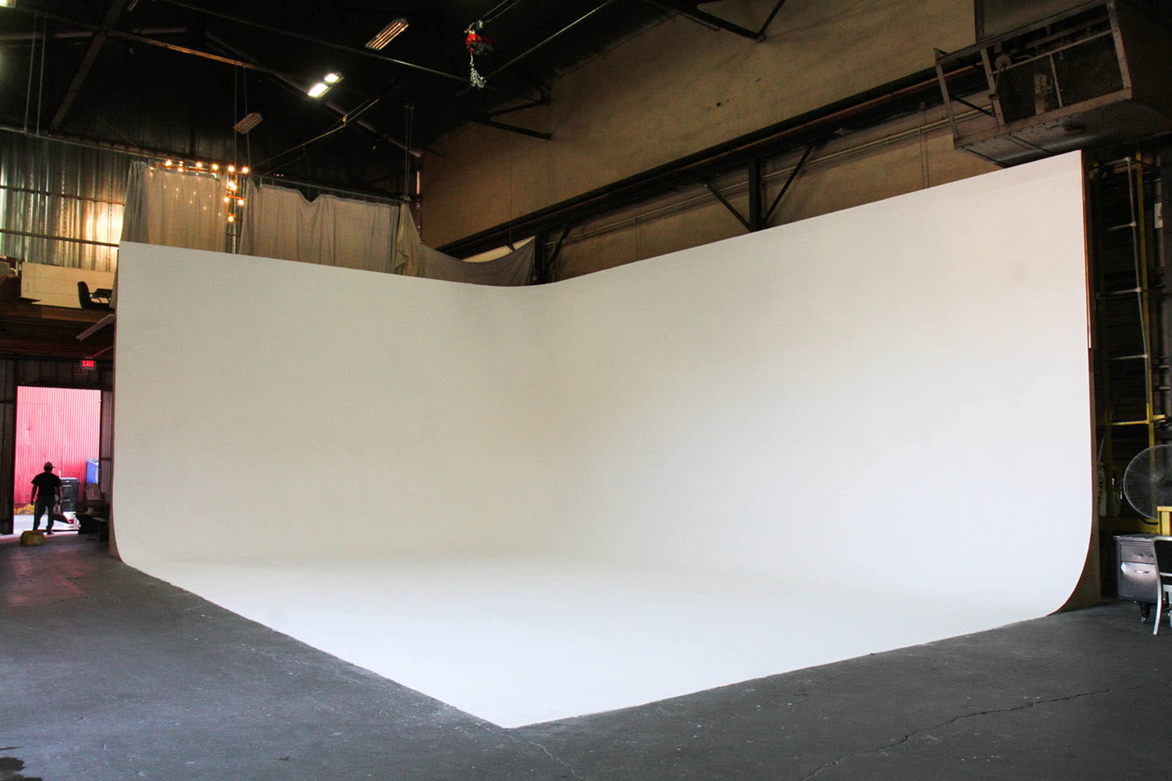 The image shows a spacious photography studio with a large white backdrop and a concrete floor.