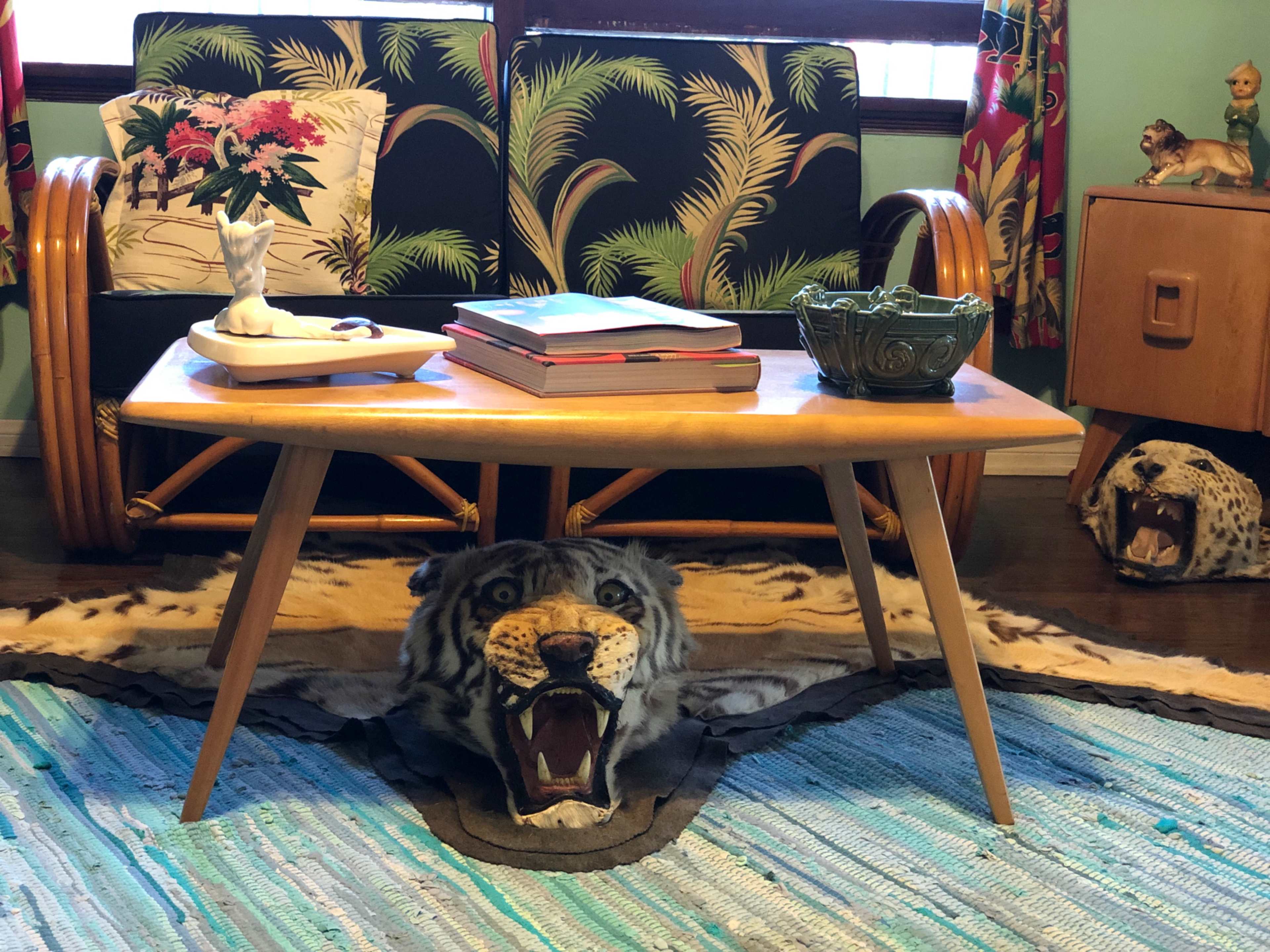 The scene features a mid-century modern coffee table atop a large tiger skin rug, surrounded by tropical-themed decor and a rattan chair.